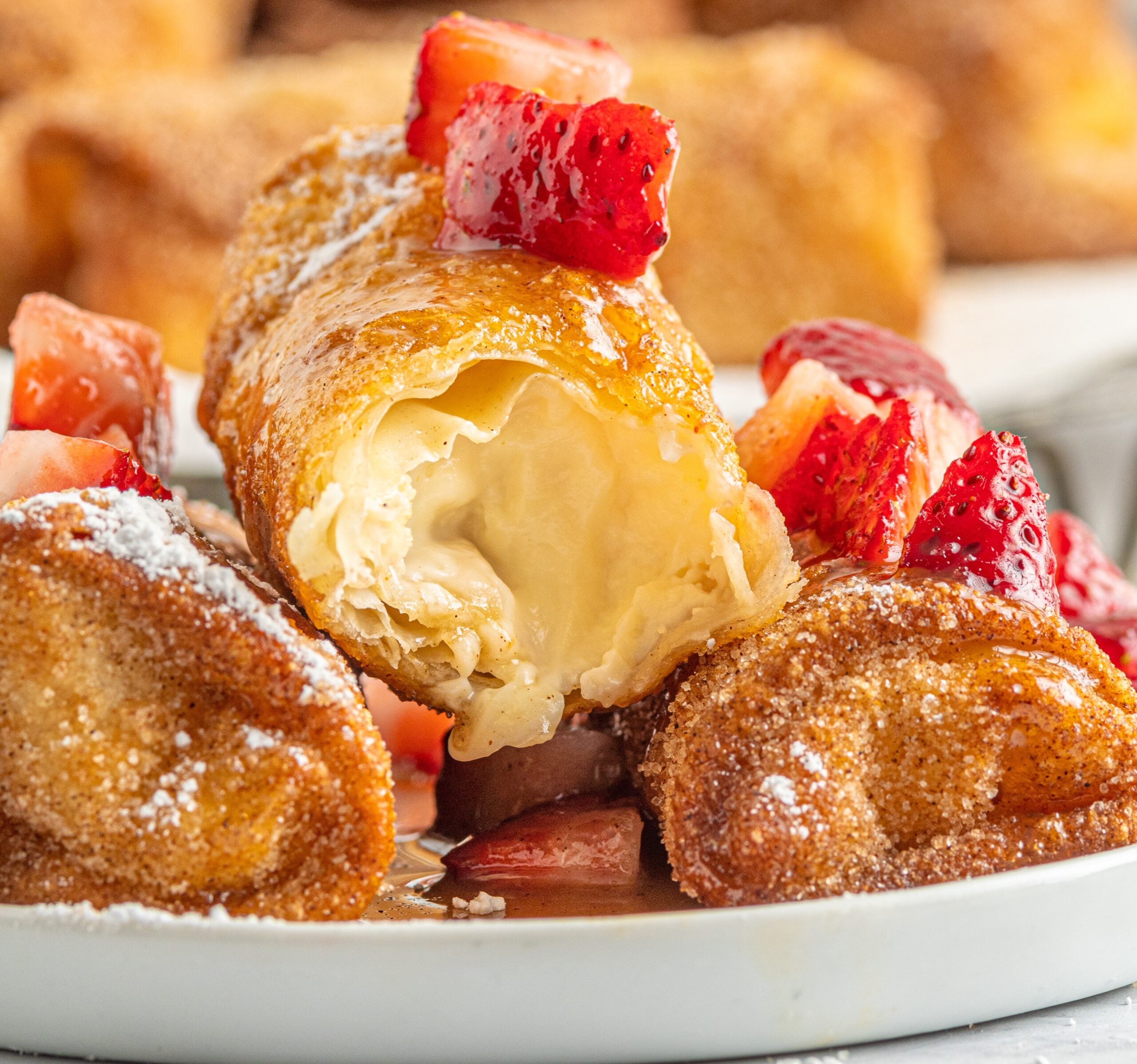 Cheesecake Eggrolls on a white plate cut open to show the filling then topped with sliced strawberries