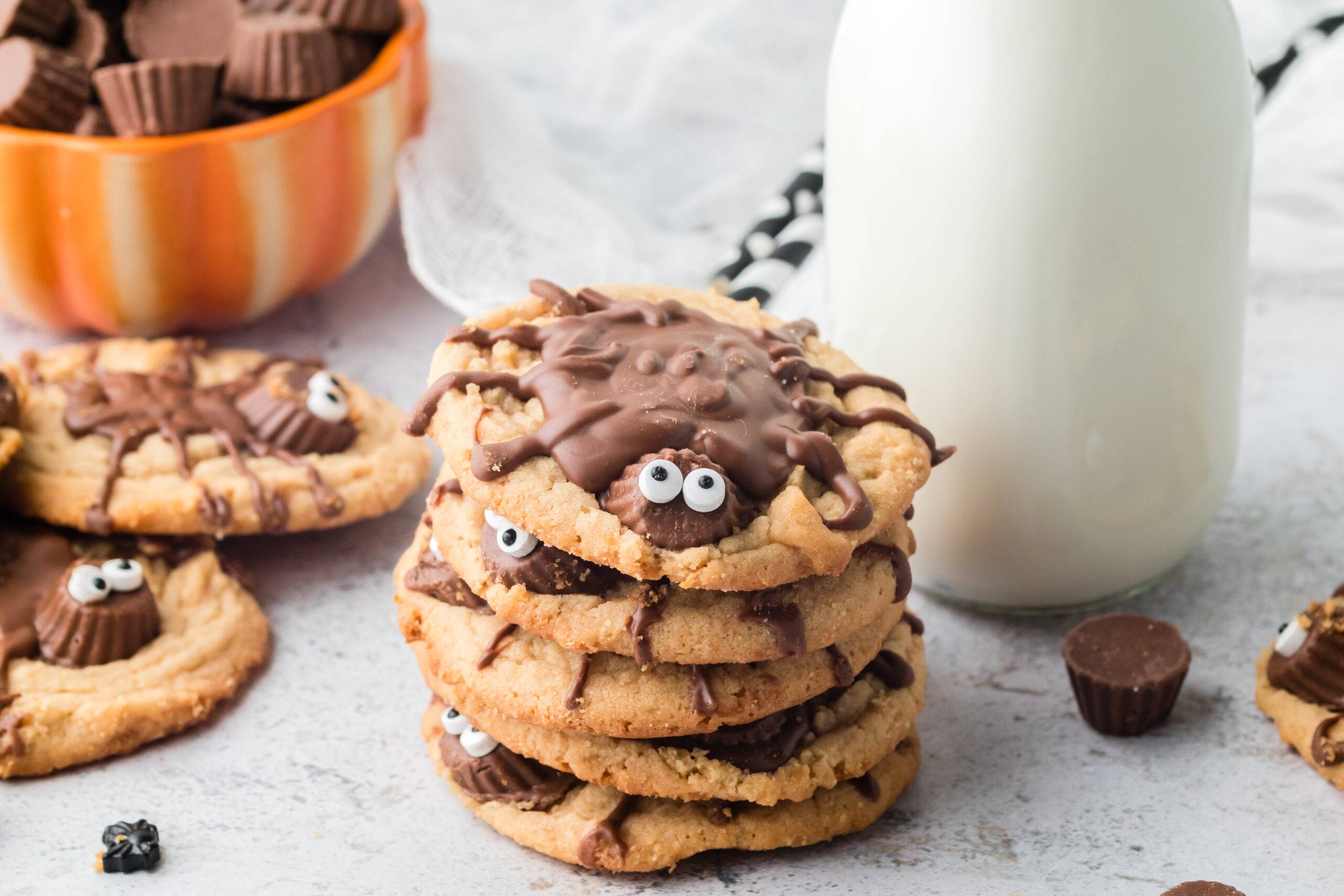 Peanut Butter Spider Cookies stacked on a table with a glass of milk next to them