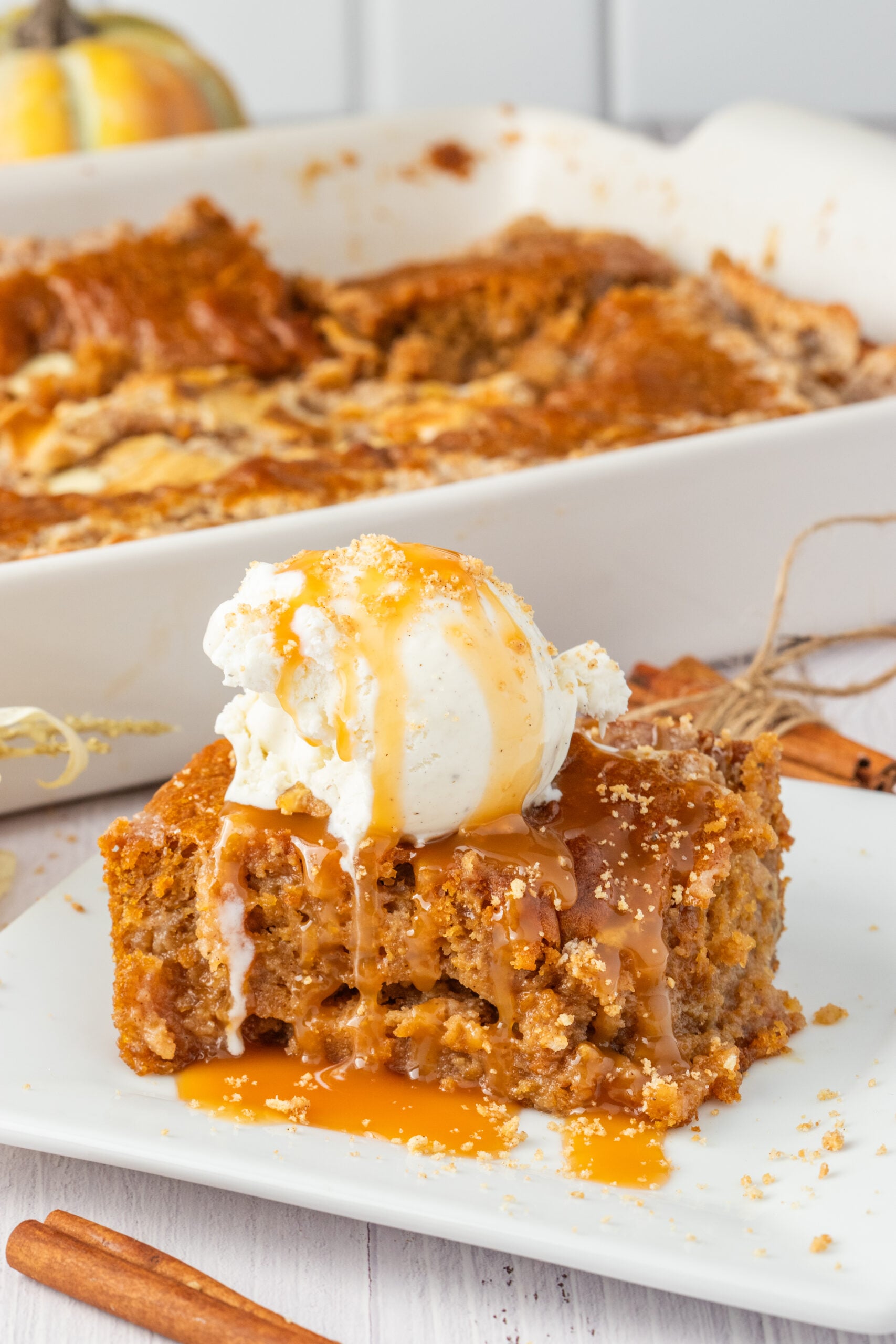 Pumpkin Earthquake Cake on a white plate with a scoop of vanilla ice cream on top then drizzled with caramel sauce