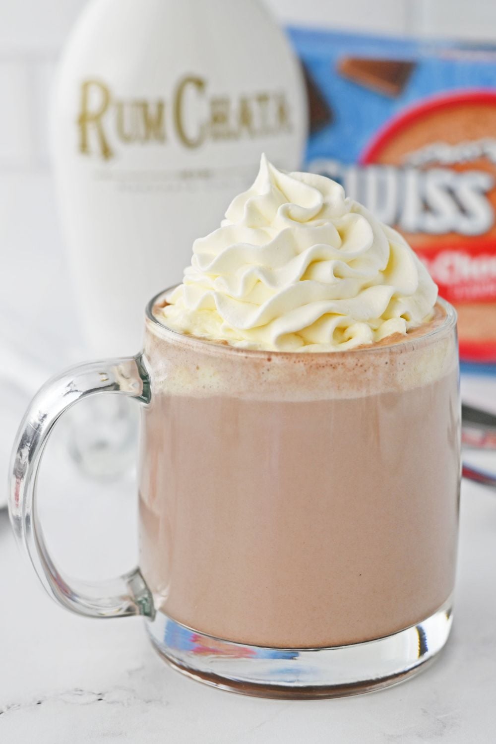 close up of hot chocolate with whipped cream on counter with a bottle of RumChata in the background