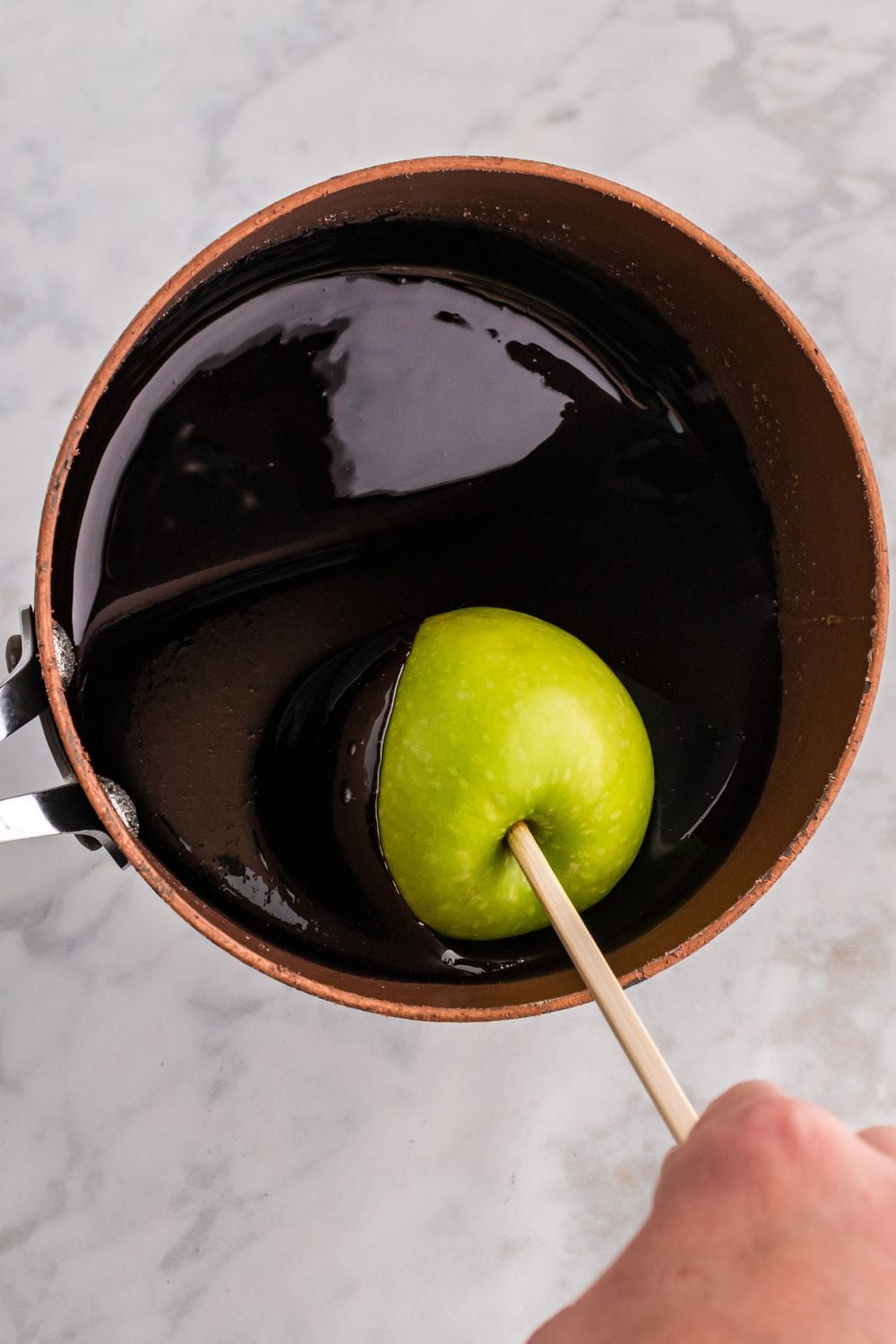 dipping apple on stick in a black candy coating