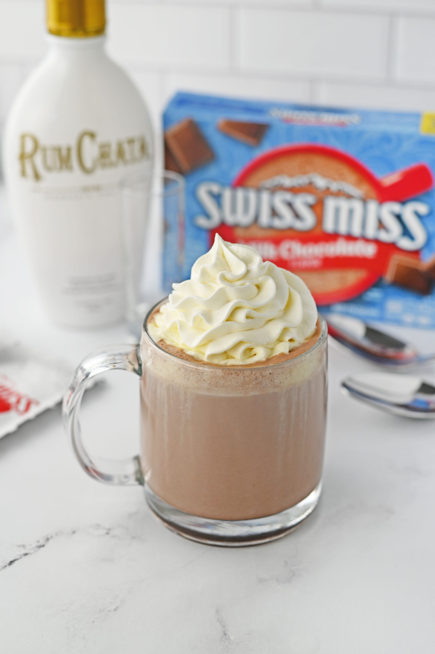 rumchata Hot Chocolate in a clear glass mug topped with whipped cream on a white marble table