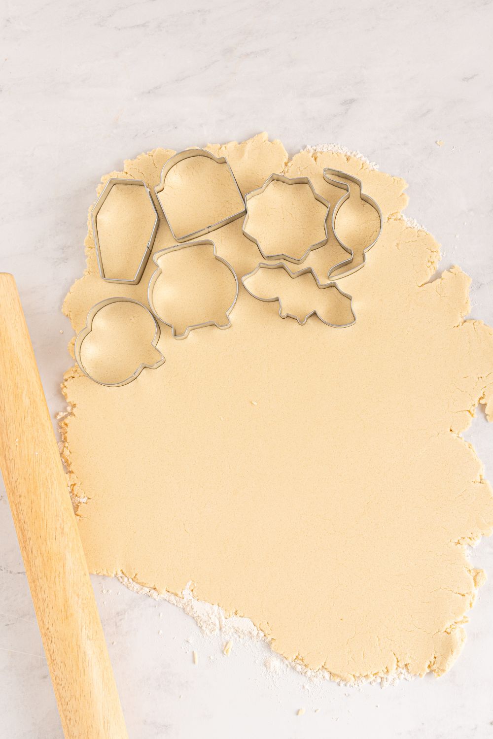 cookie cutters on sugar cookie dough as it is rolled out on table 
