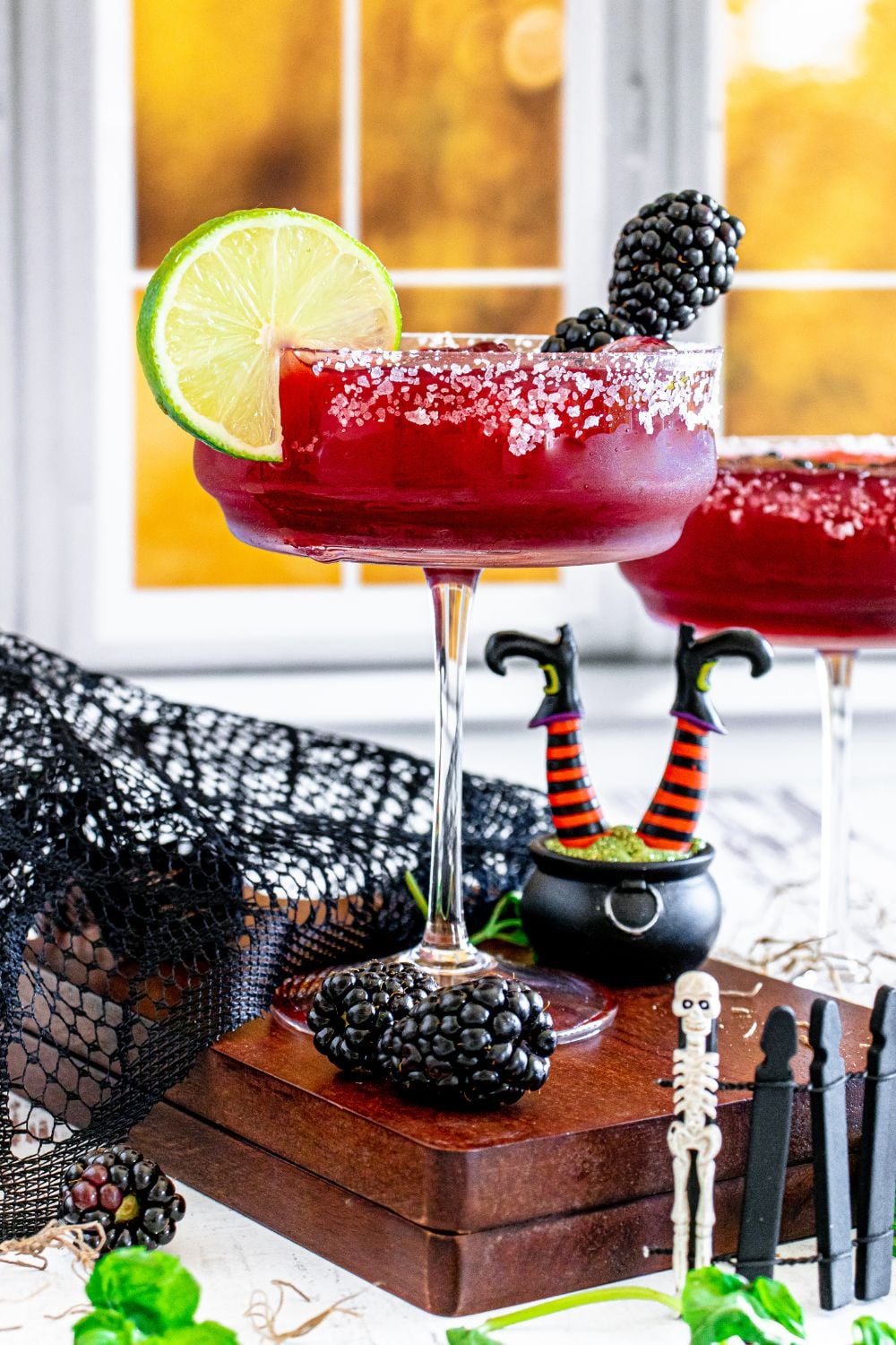 hocus pocus blackberry margarita in glasses on table with halloween decor around it
