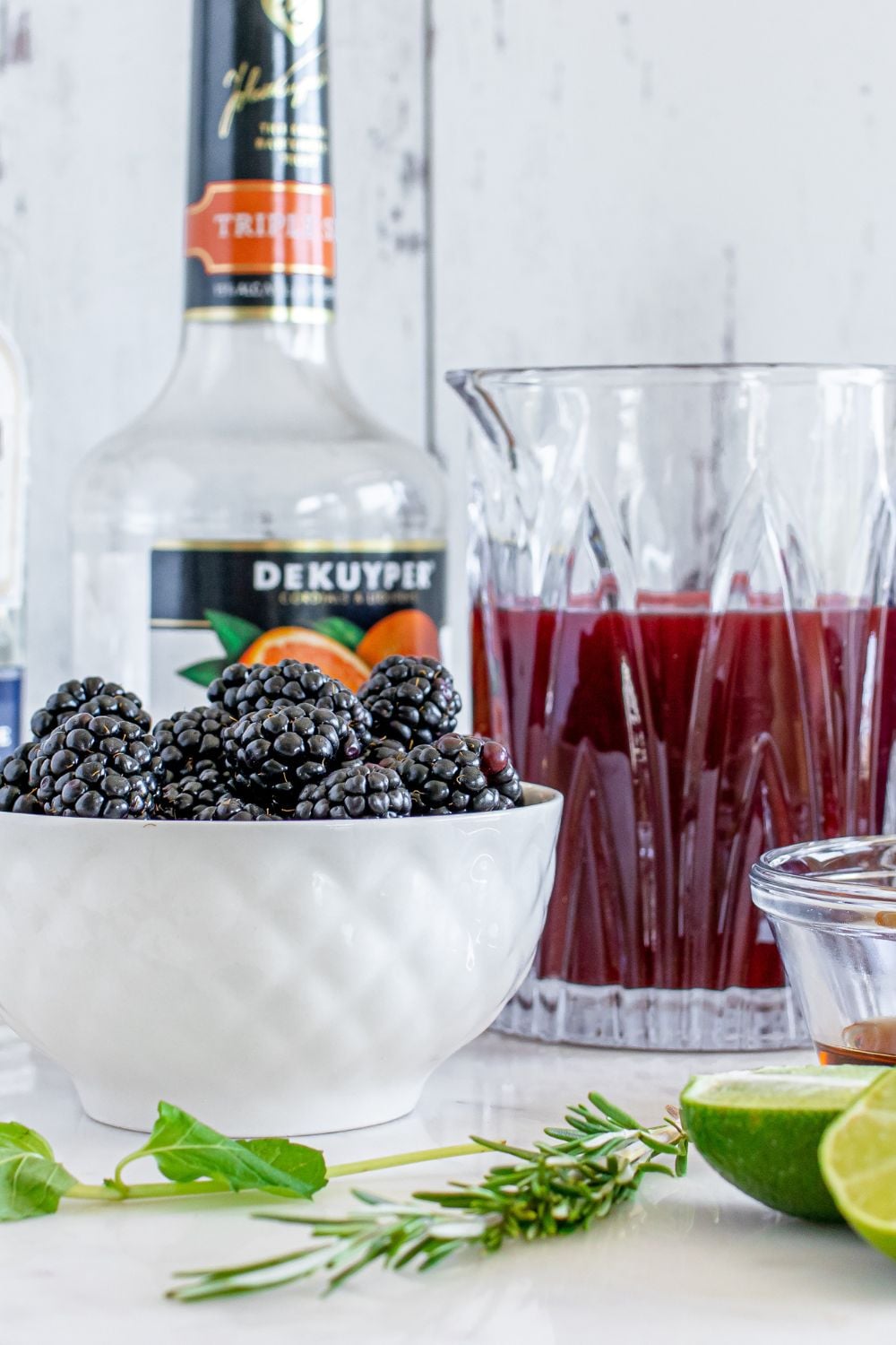 blackberries in a bowl, glass with juice, sliced limes and more on table