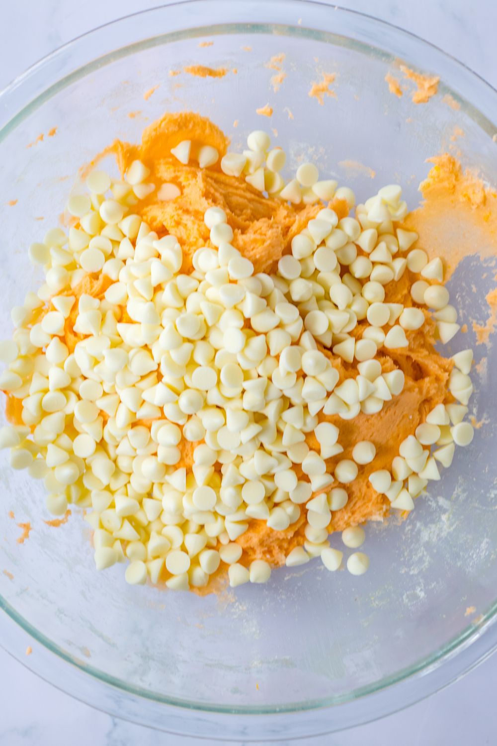 white chocolate chips on top of a orange cookie batter in bowl 