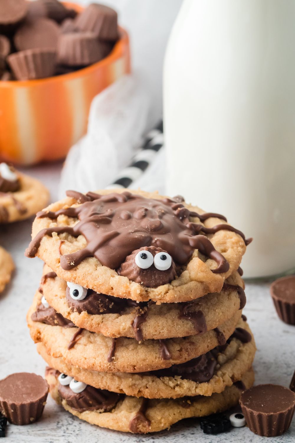 stacked cookies that look like spiders on table with milk behind it in a glass jar