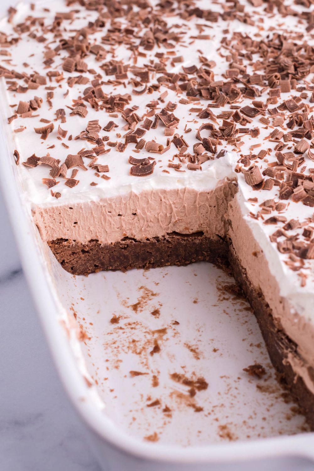 layered brownie dessert in pan with some pieces cut out to showcase the layers