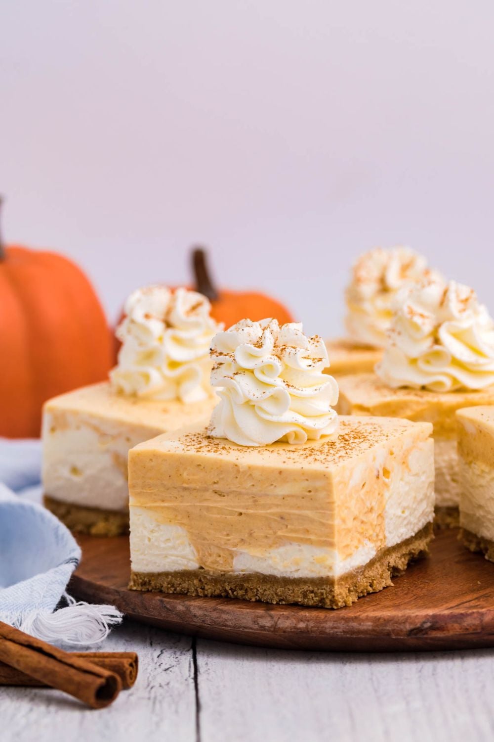 pumpkin cheesecake bars on a table with pumpkin behind it