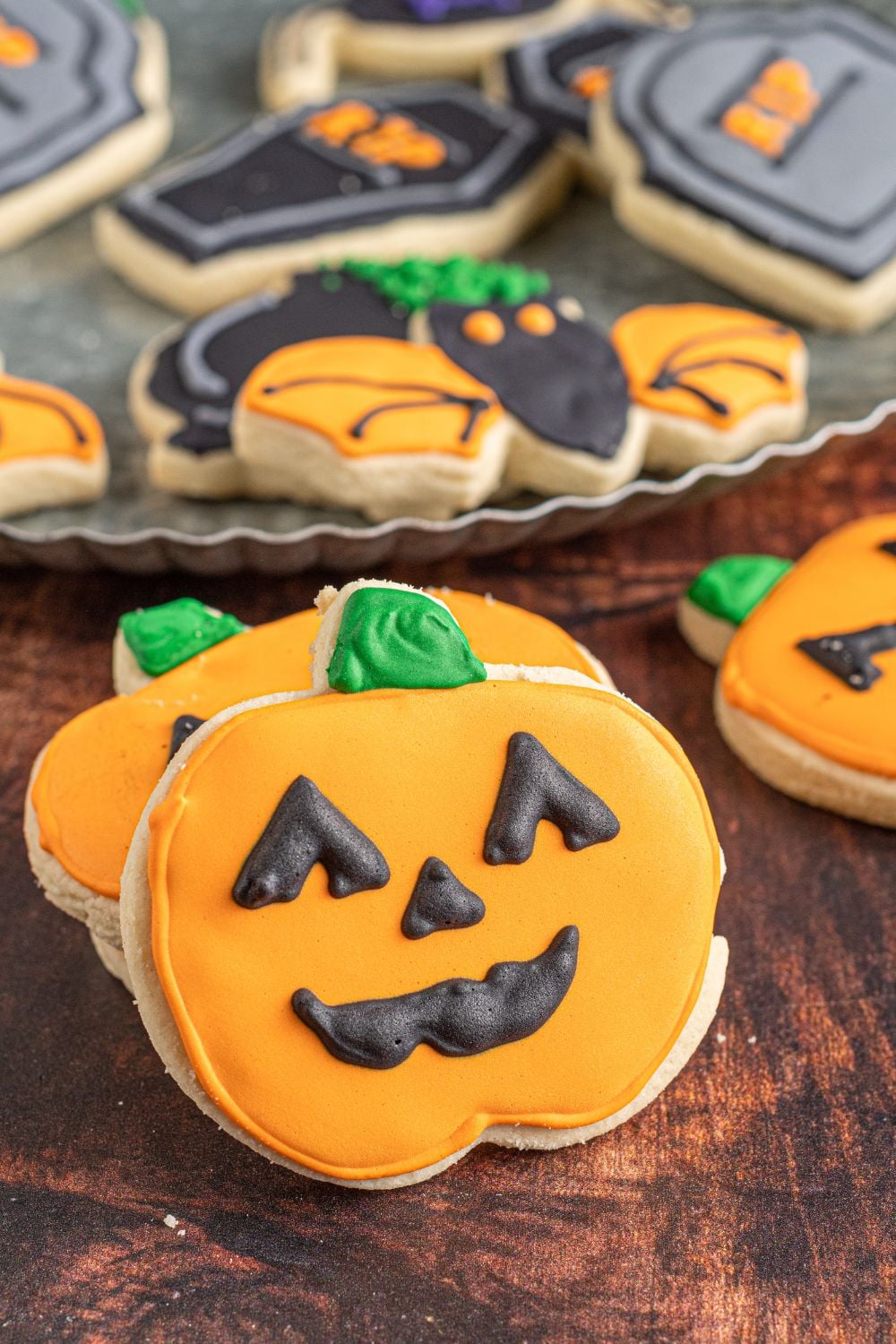 pumpkin cookies on table with a platter of cookies behind it