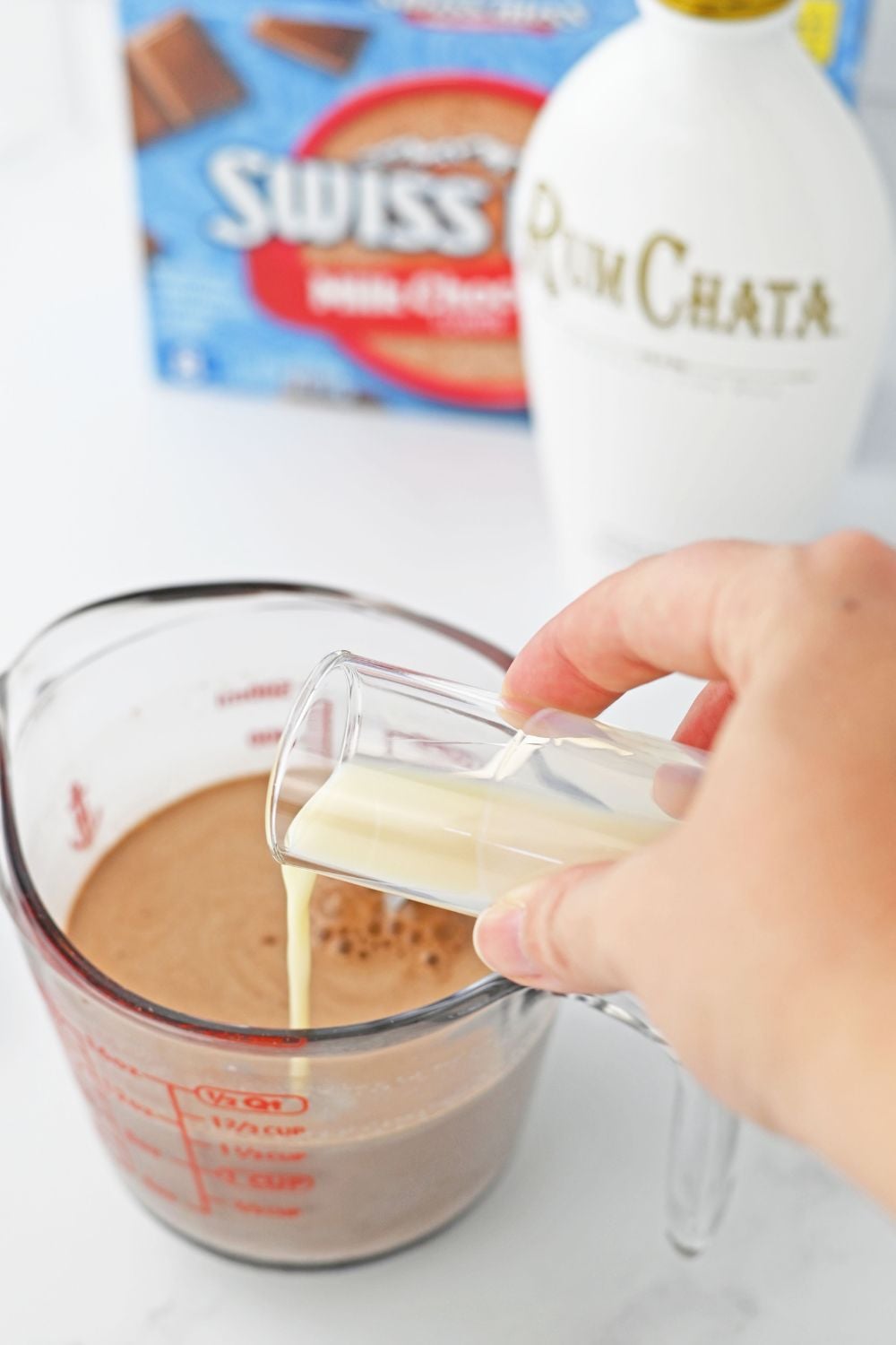 pouring rumchata into a measuring cup with hot chocolate