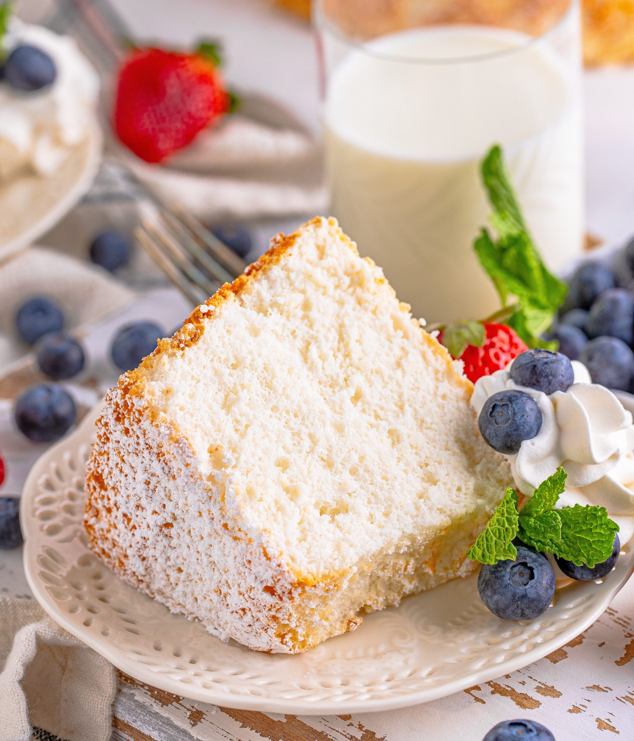 Angel Food Cake on a white plate with whipped cream, blueberries, strawberries, and mint