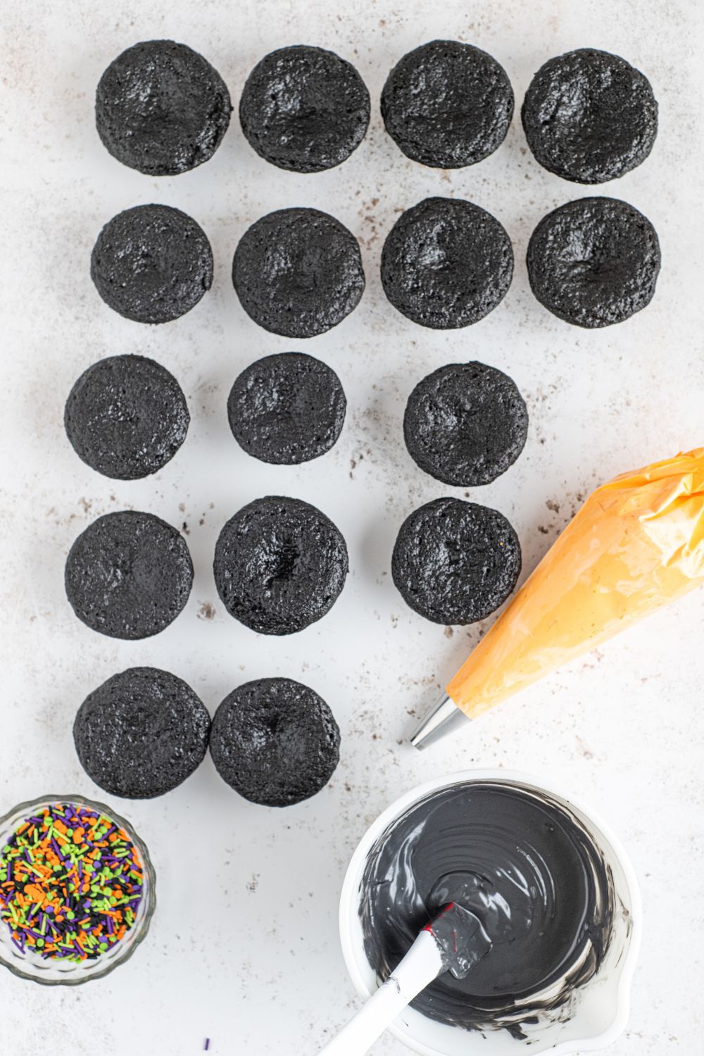 black cupcakes on counter with orange frosting on the side