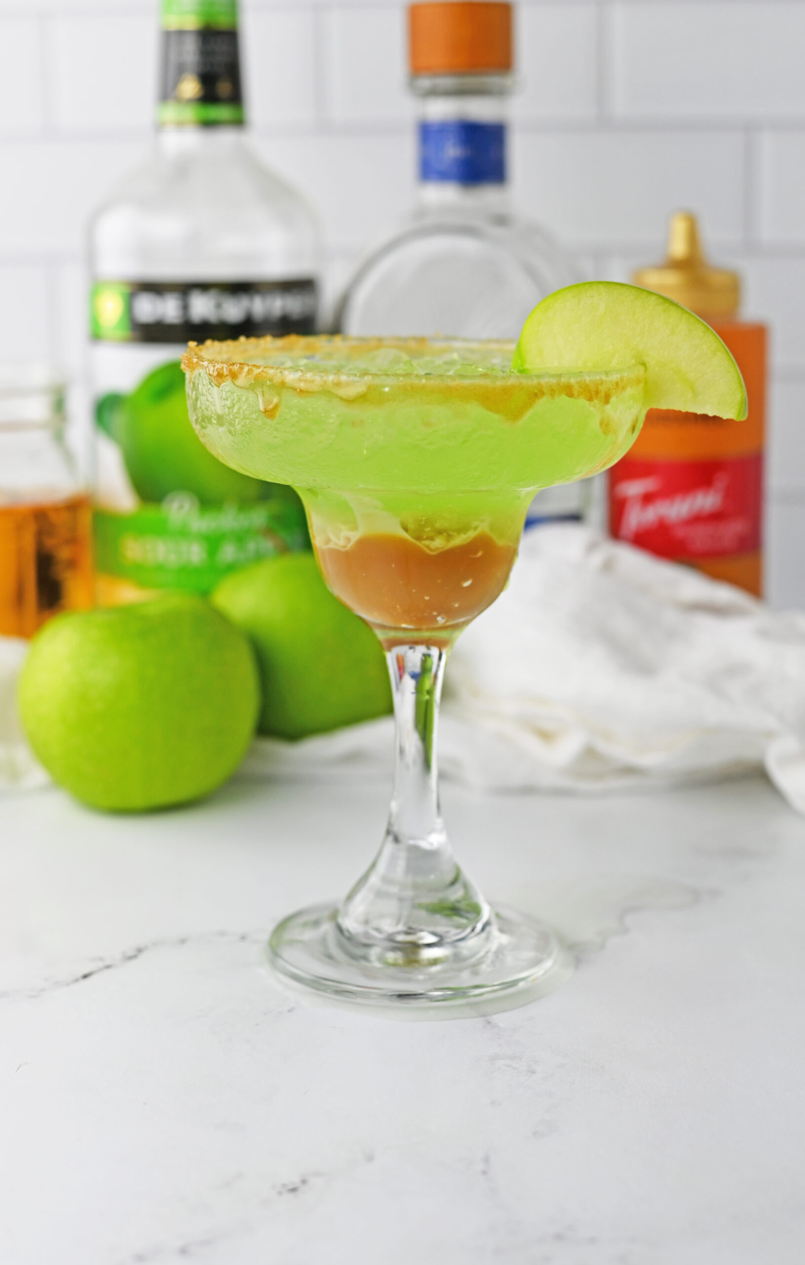 side view of caramel apple drink on table with apples behind it