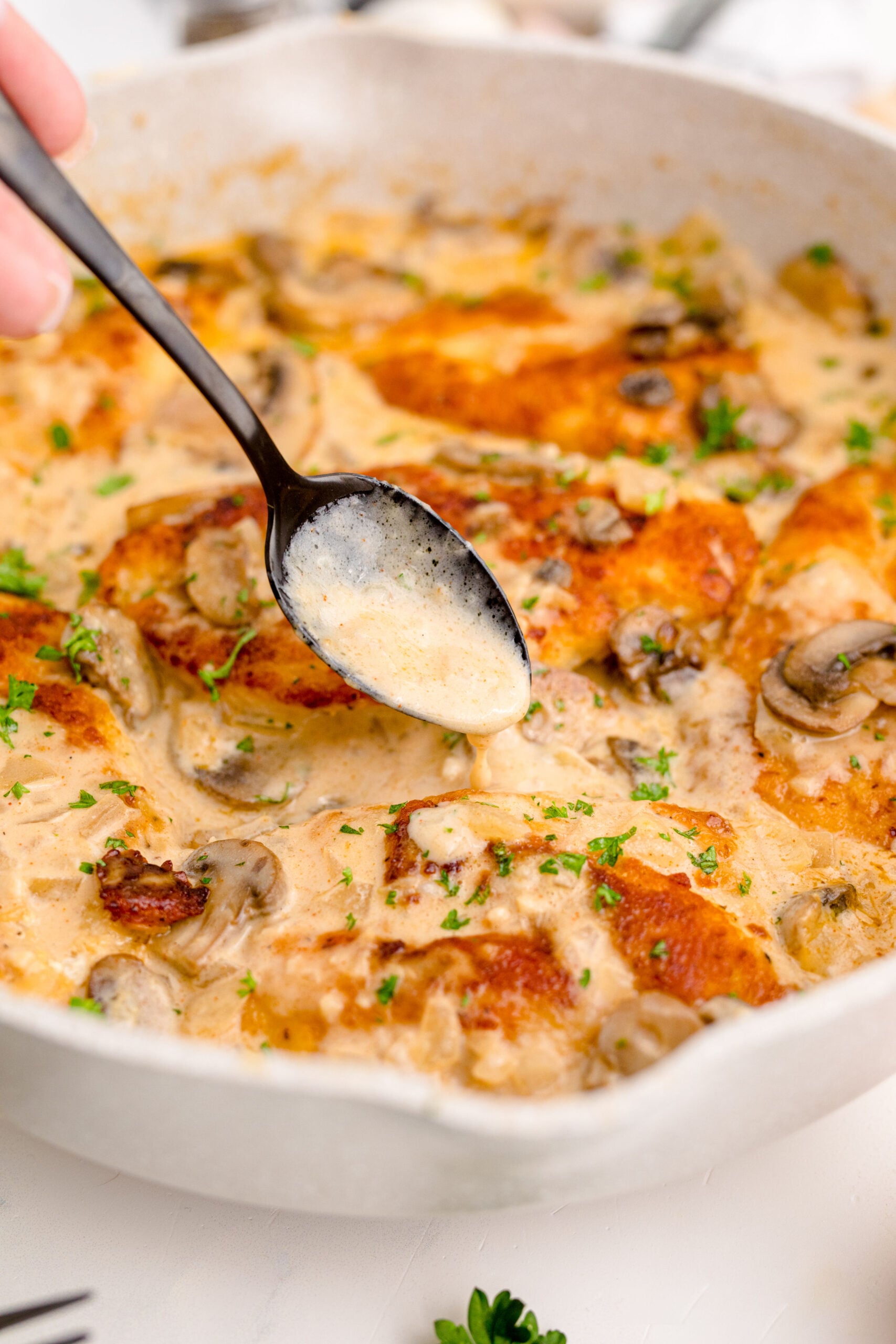 Chicken Marsala in a white skillet with a spoon pouring sauce over a piece of chicken 