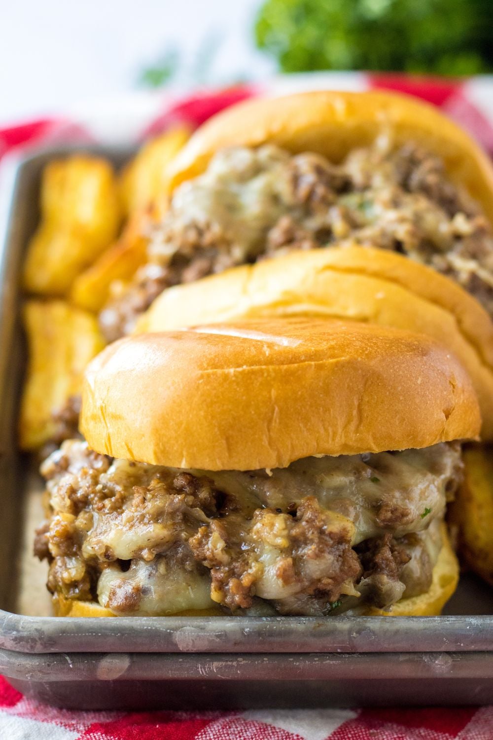 french dip sandwiches on a metal tray with potato wedges behind it 