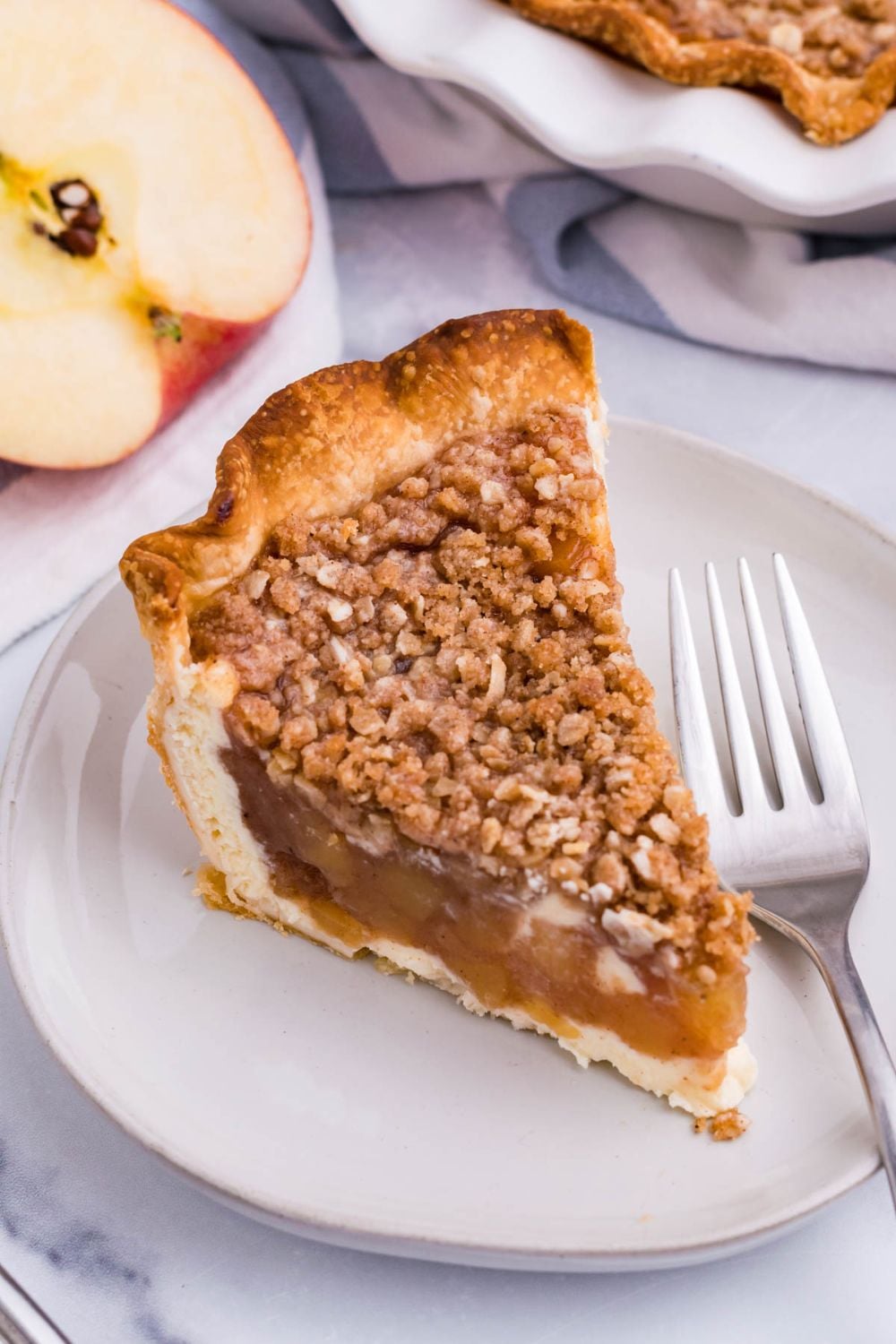 apple crumble cheesecake slice on plate with fork and apple on the side
