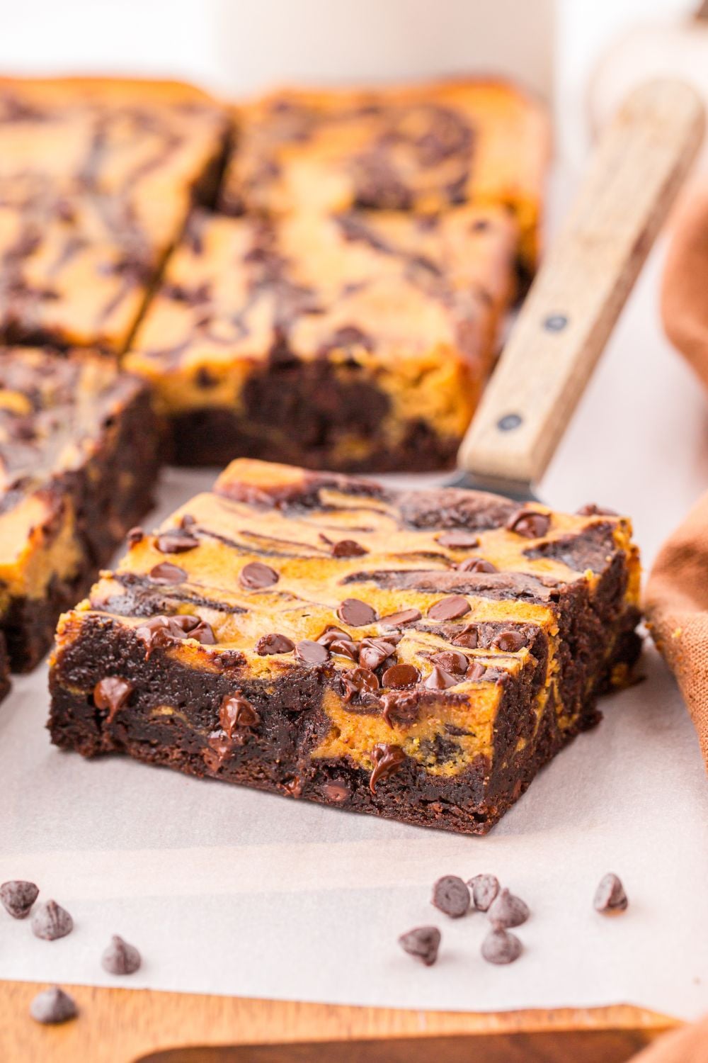 brownie slice on table with a spatula under it with chocolate chips around it on table