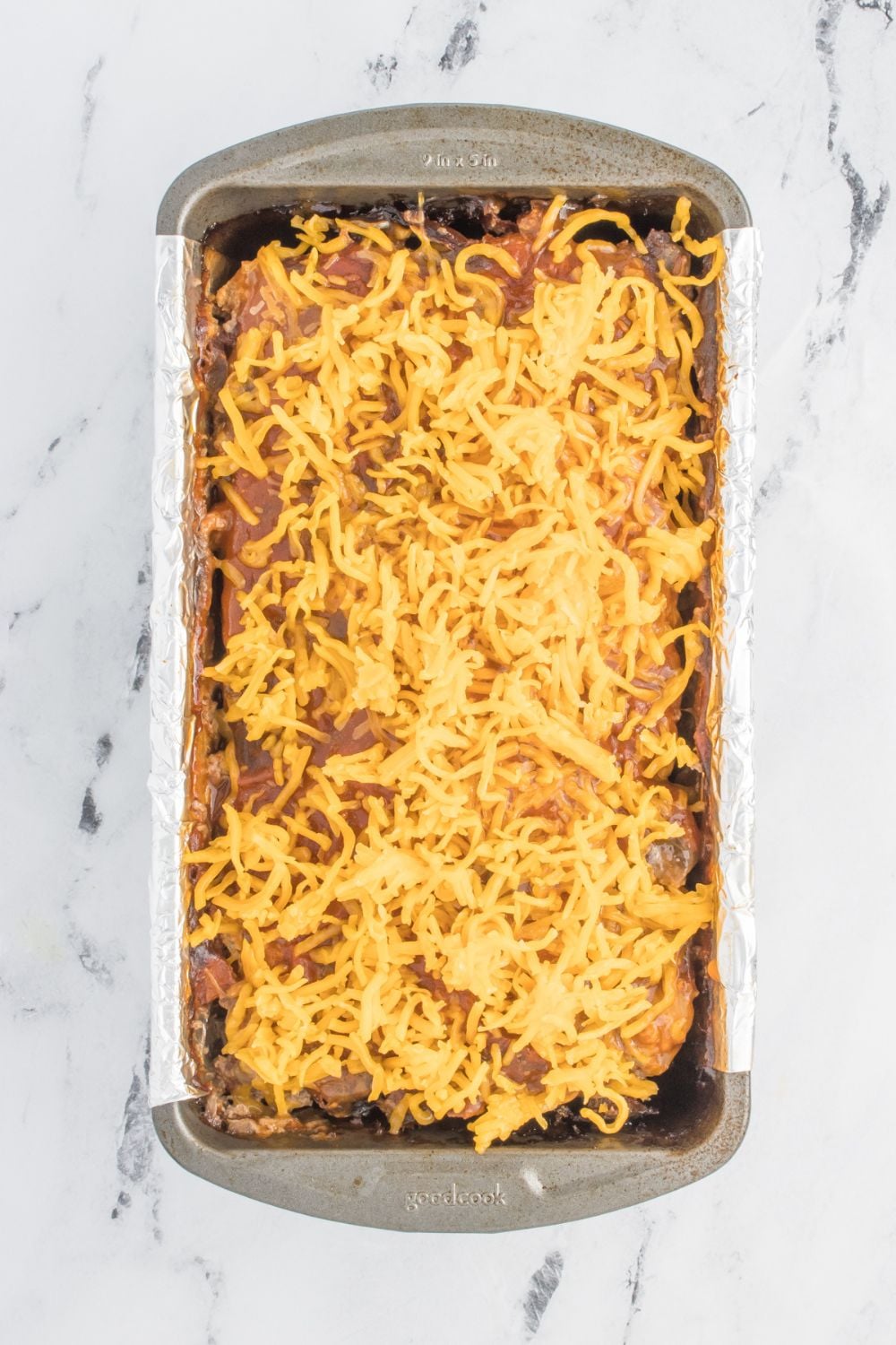 raw meatloaf in a pan with shredded cheese