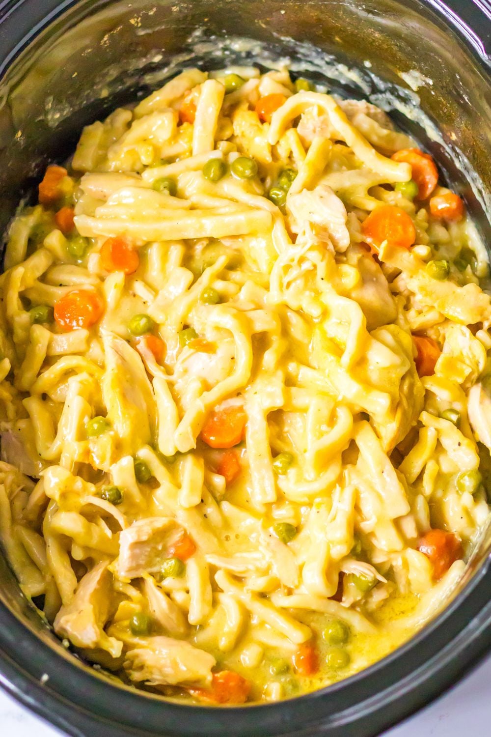 overhead shot of chicken and noodles in a slow cooker on table