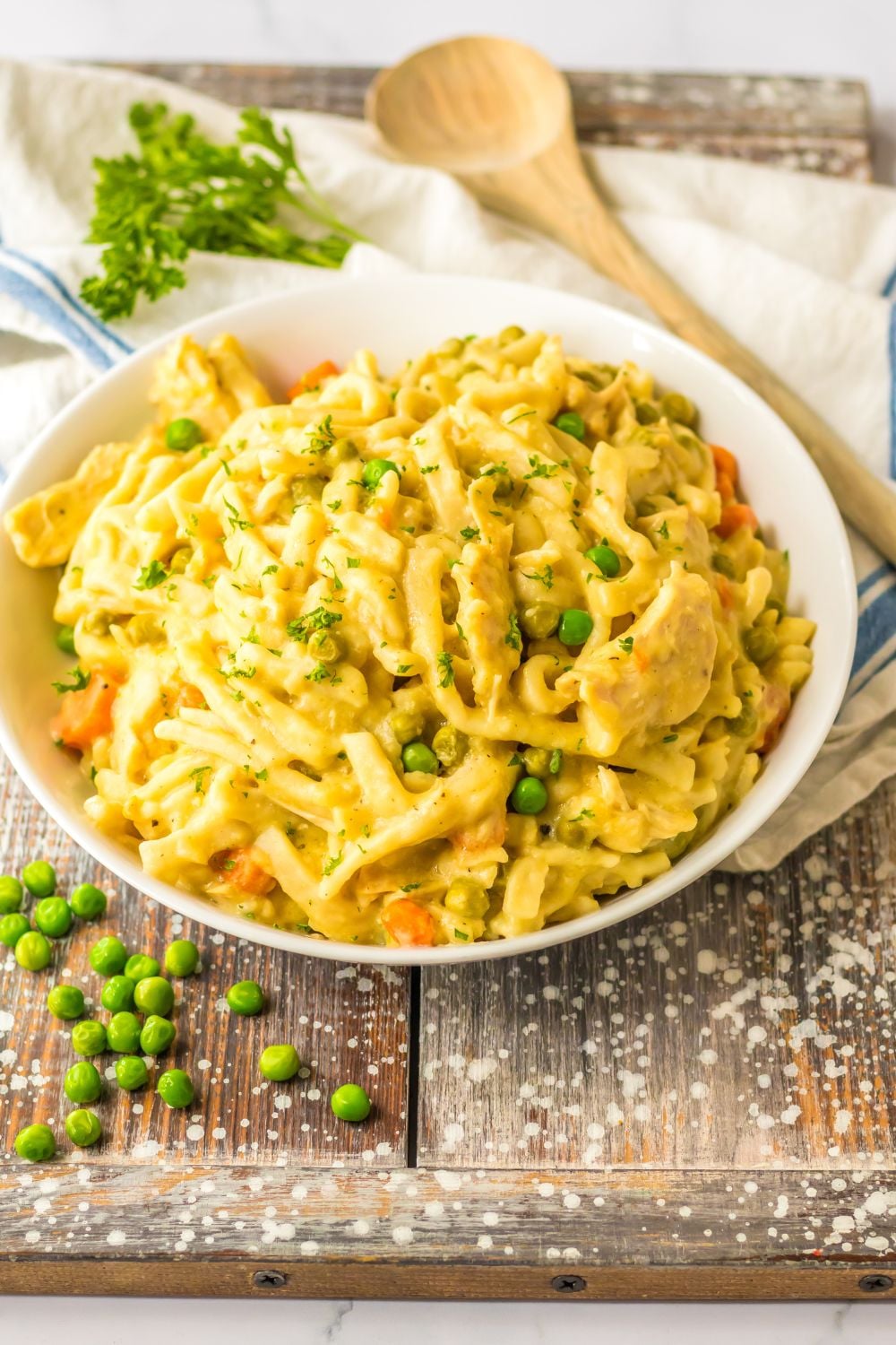 chicken noodles in a bowl with peas on table and wooden spoon behind it