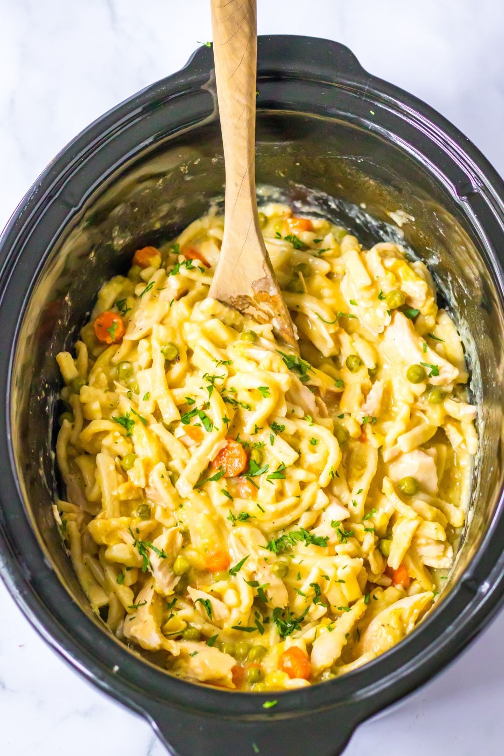 crockpot chicken noodle soup in a crockpot with a wooden spoon in it