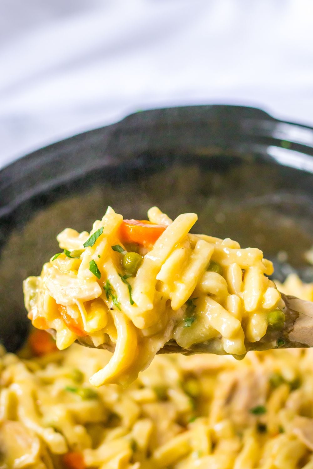 chicken and noodles on a wooden spoon above crockpot