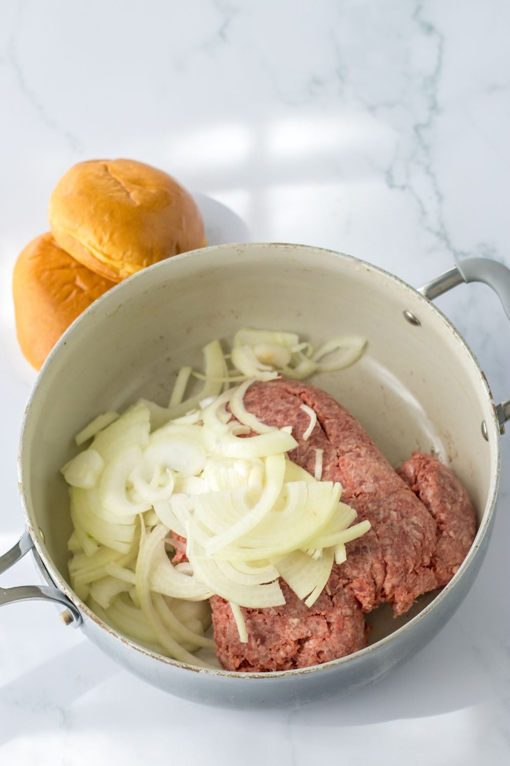 raw ground beef and sliced onions in a pan on stovetop