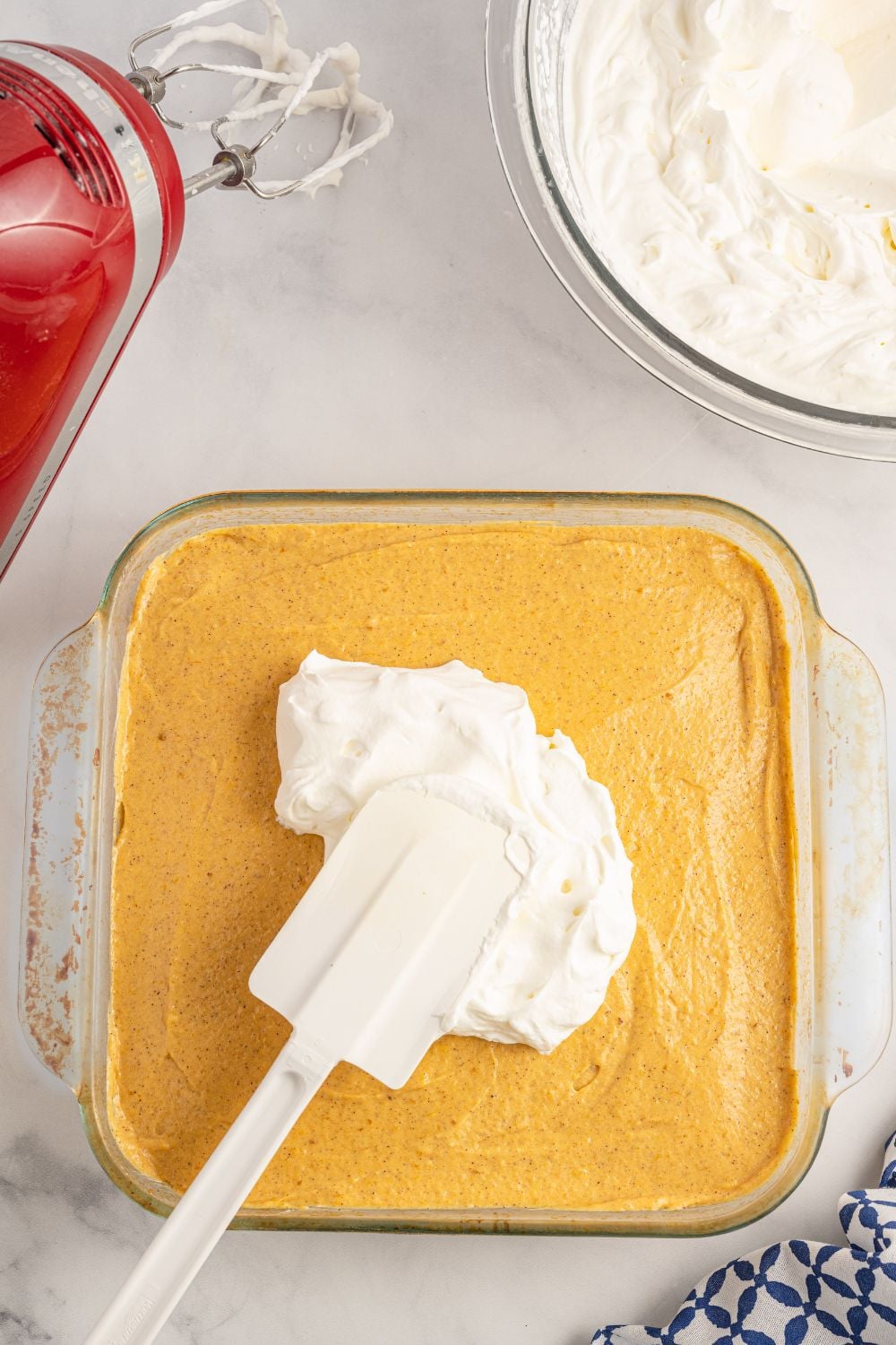 spreading whipped cream over the top of a pumpkin layered dessert