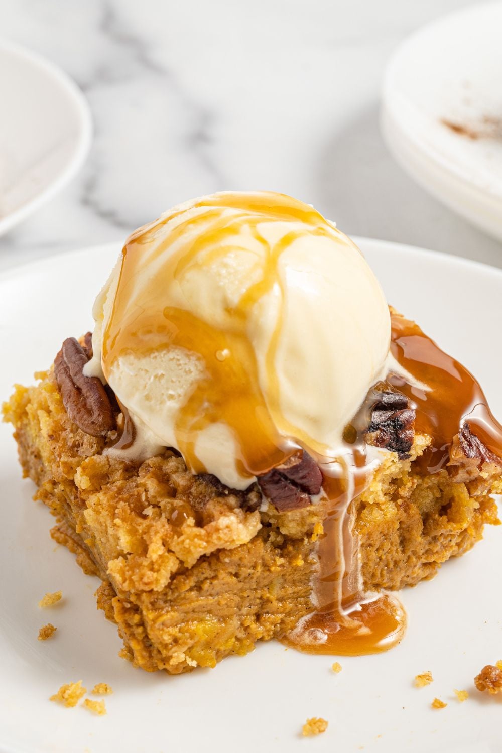 slice of pumpkin cake on plate with scoop of ice cream and caramel sauce on top