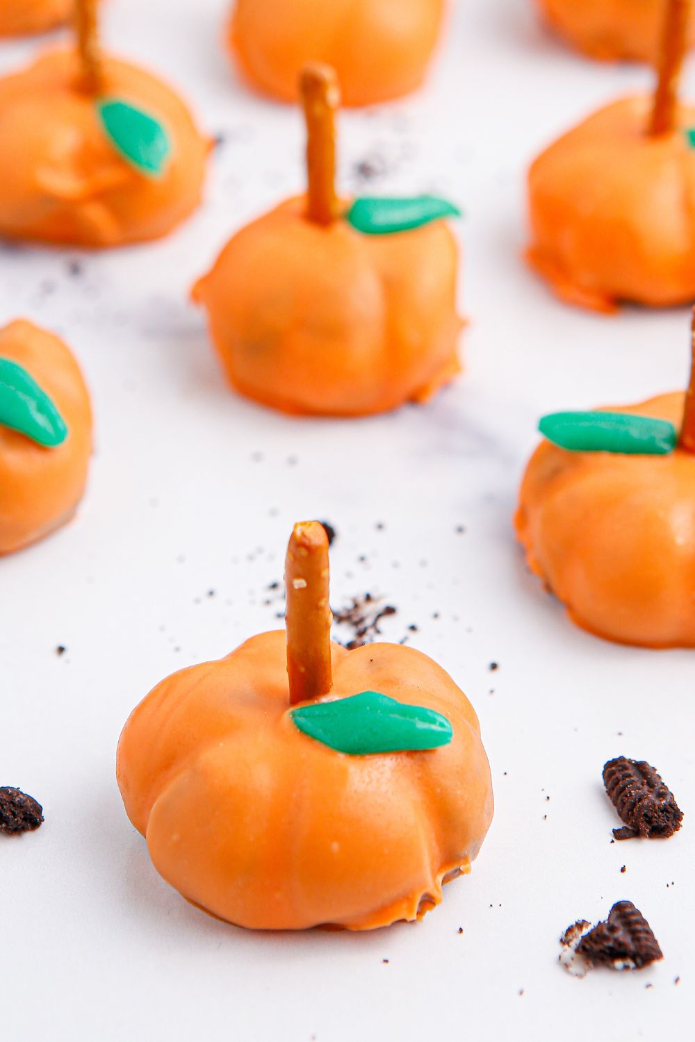 pumpkin oreo cheesecake bites on white table with cookie crumbles around it