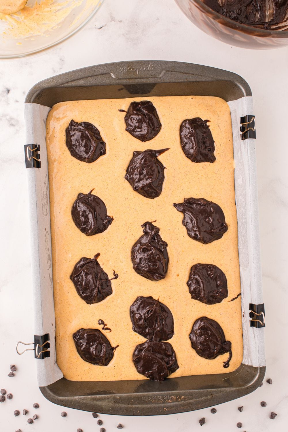pumpkin cheesecake brownie batter in a pan with drop of chocolate brownie mixture