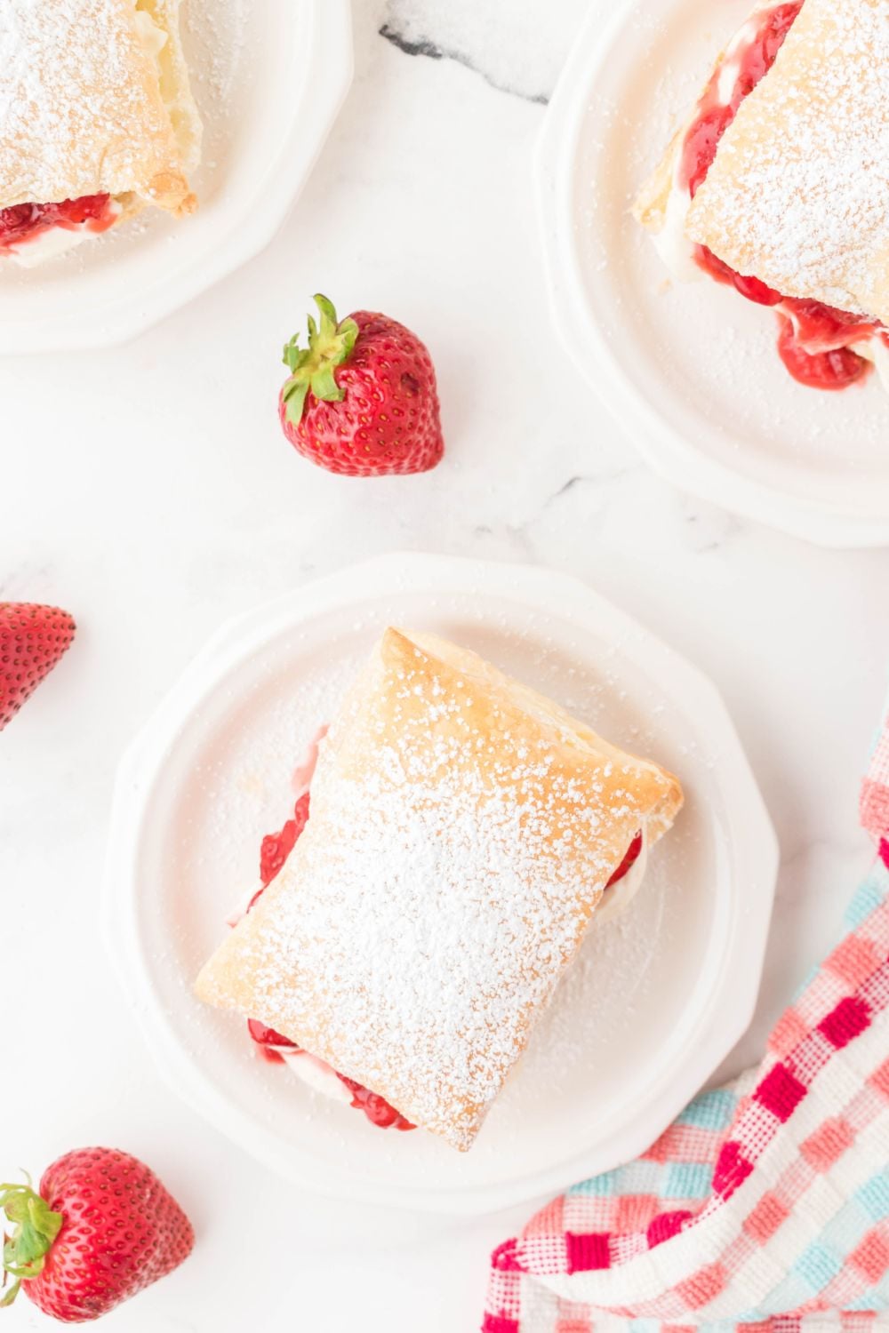 strawberries puff pastries on plates with berries around it on table