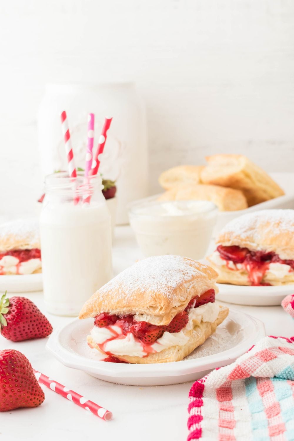strawberry shortcake puffs on plates with a jar of milk and paper straws in it