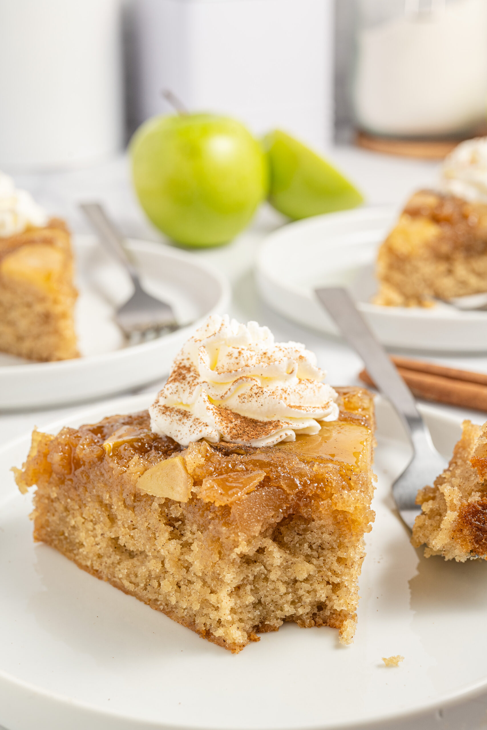 bite taken out of apple spice cake on plate with whipped cream on top