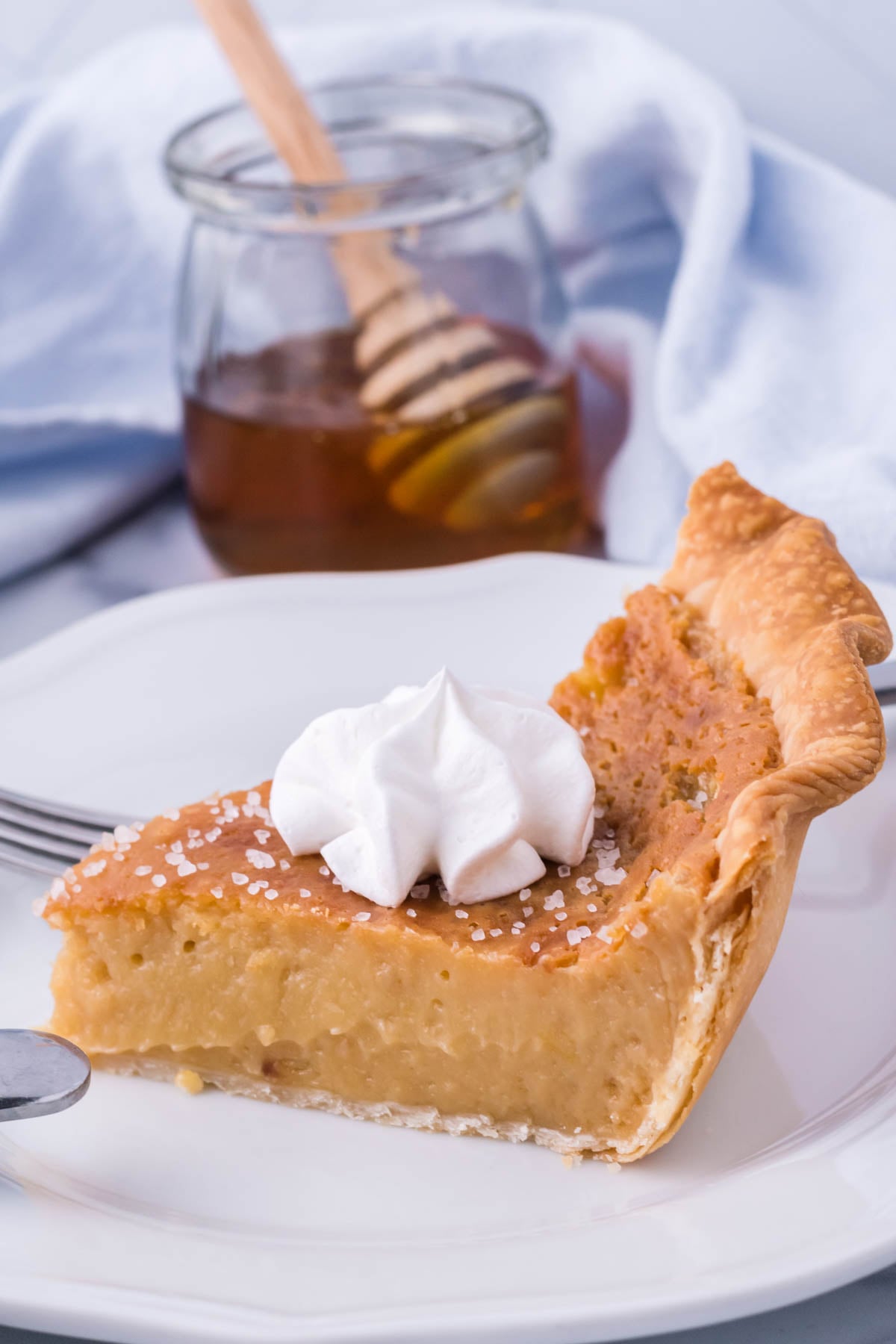 up close side shot of honey pie on a white plate with a clear jar of raw honey behind it