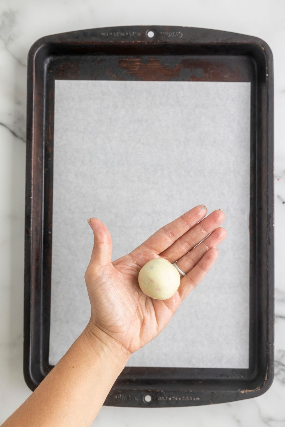 rolled truffle dough in hand above a metal baking tray 