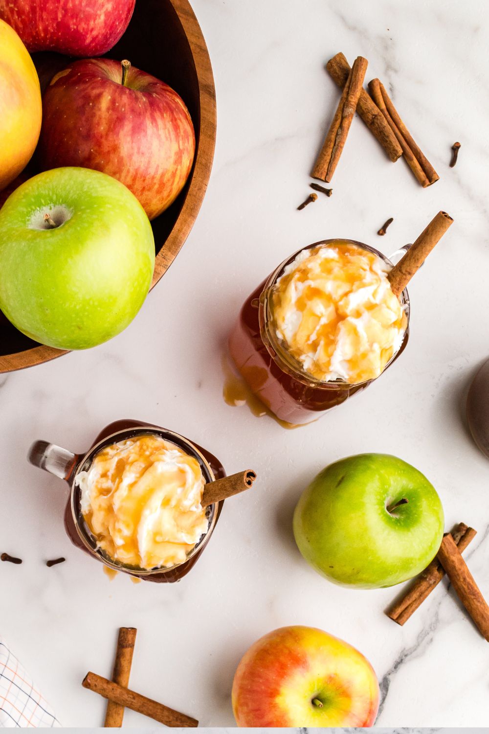 glasses of cider on table with apples and cinnamon sticks around it