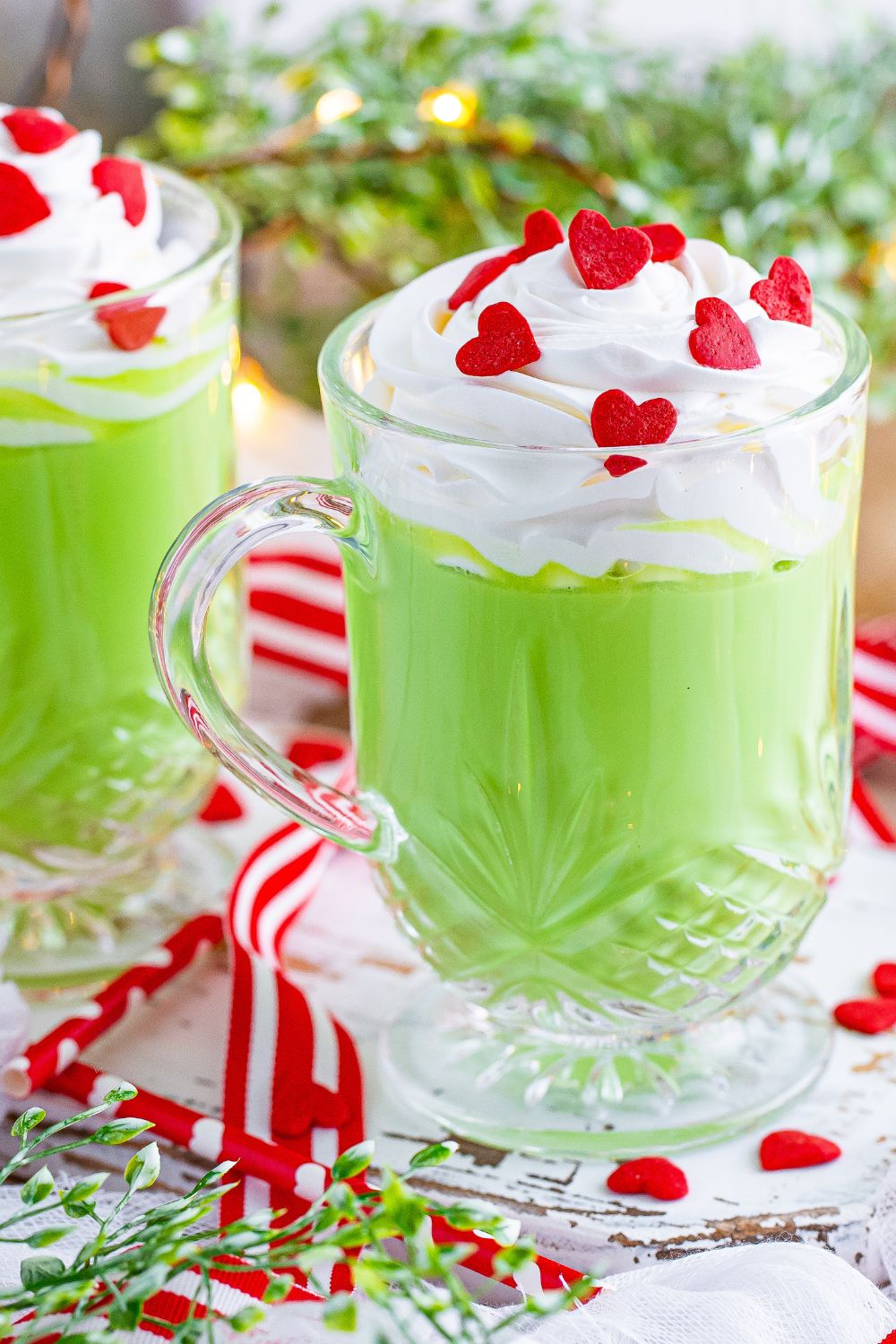 grinch hot chocolate in glass mugs on table with tree behind it
