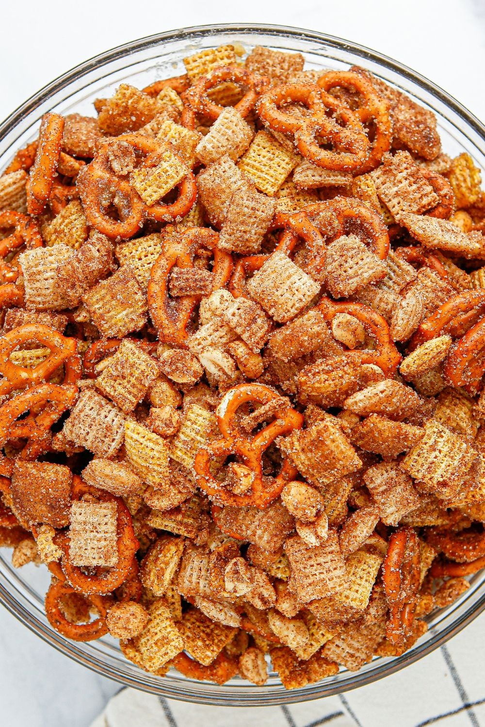 chex mix in a glass bowl on table with towel under it