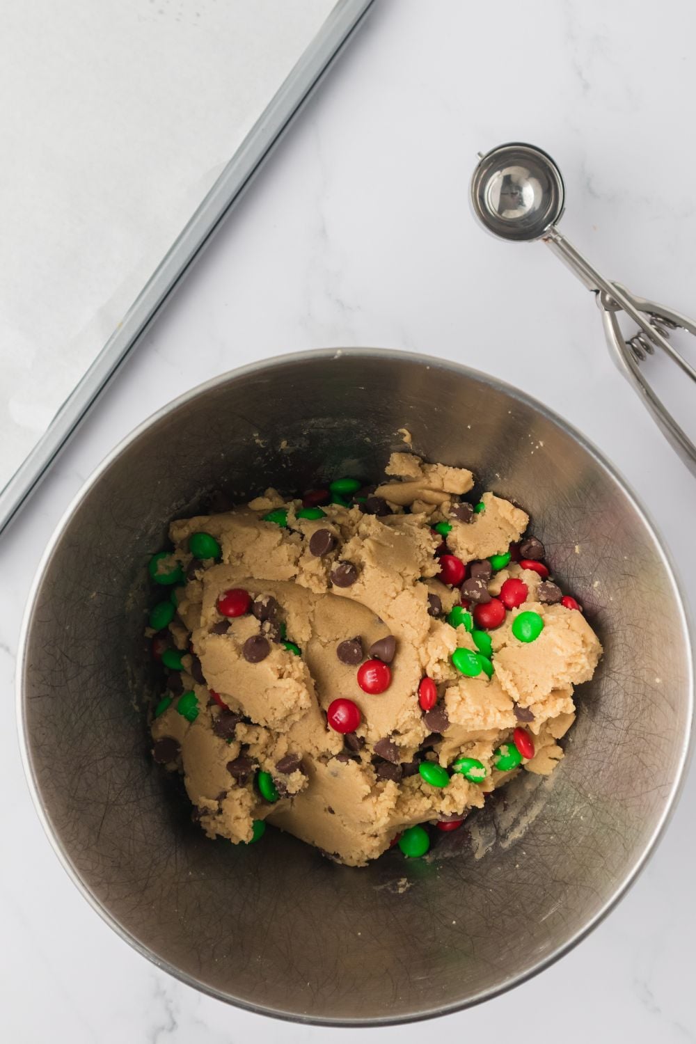 chocolate chips and m&Ms sprinkled on top of cookie dough in mixer bowl