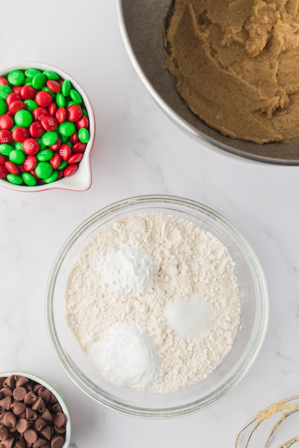 flour in a bowl with salt and other items i it, with cookie dough ingredients around it on table