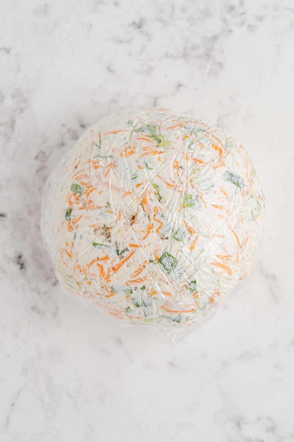 cheese ball wrapped in plastic wrap on table