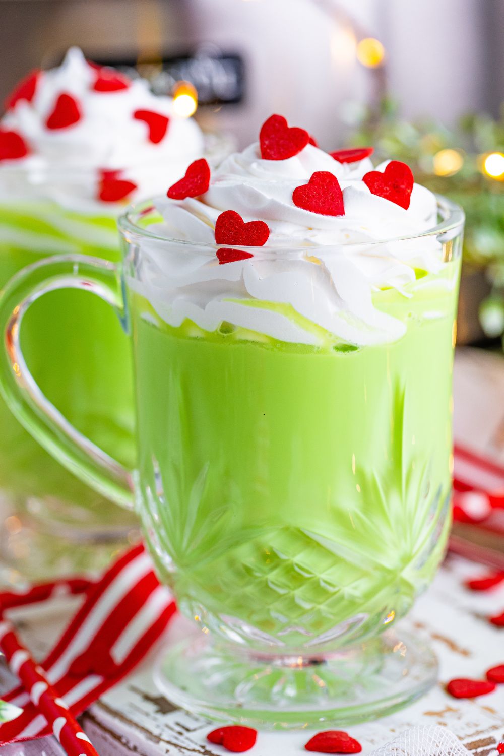 glasses of green colored hot cohcolate and whipped cream and red heart sprinkles in mugs