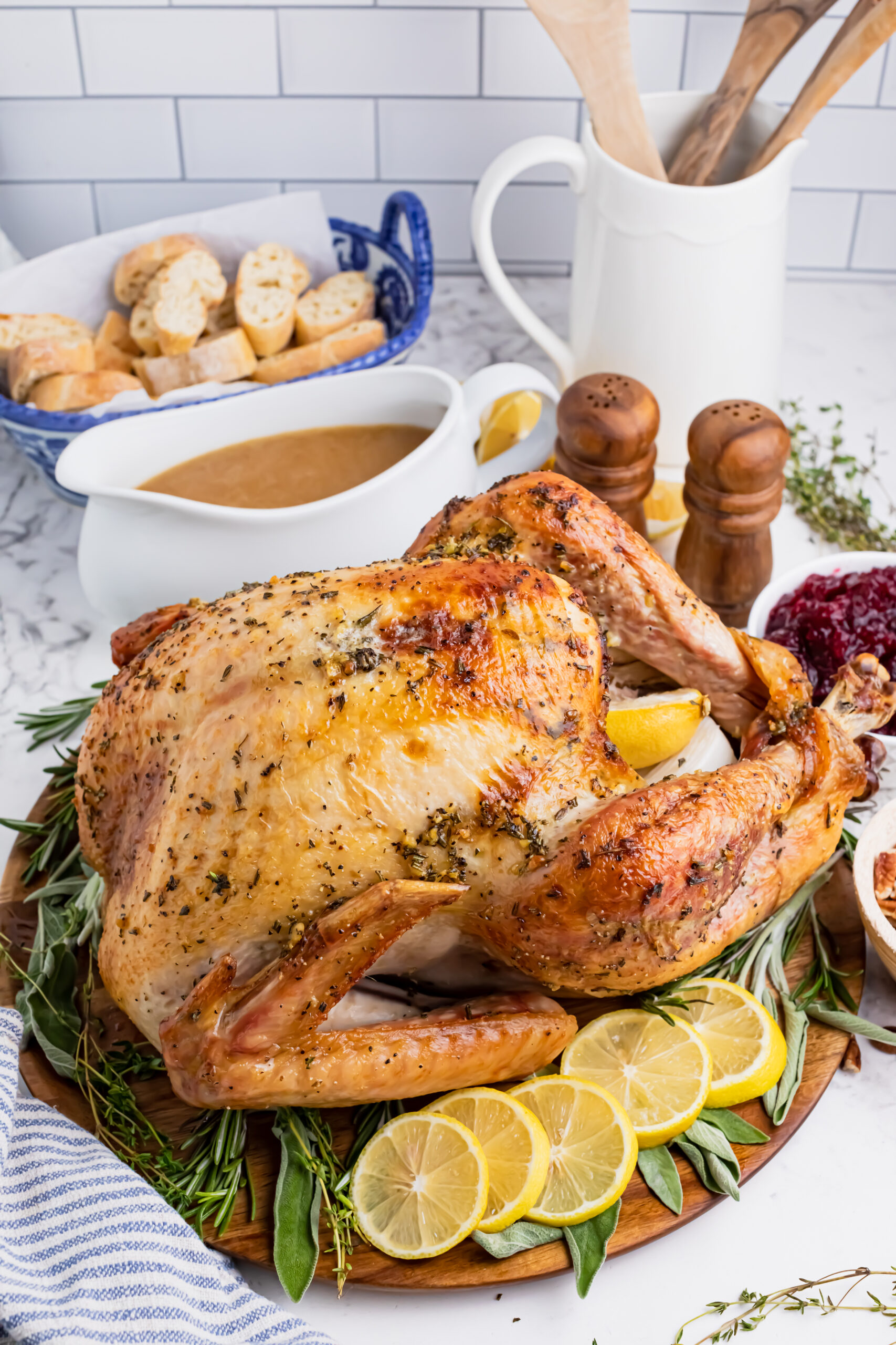 Roasted turkey on a wooden cutting board with gravy in a white bowl and cranberry sauce in another bowl in the background