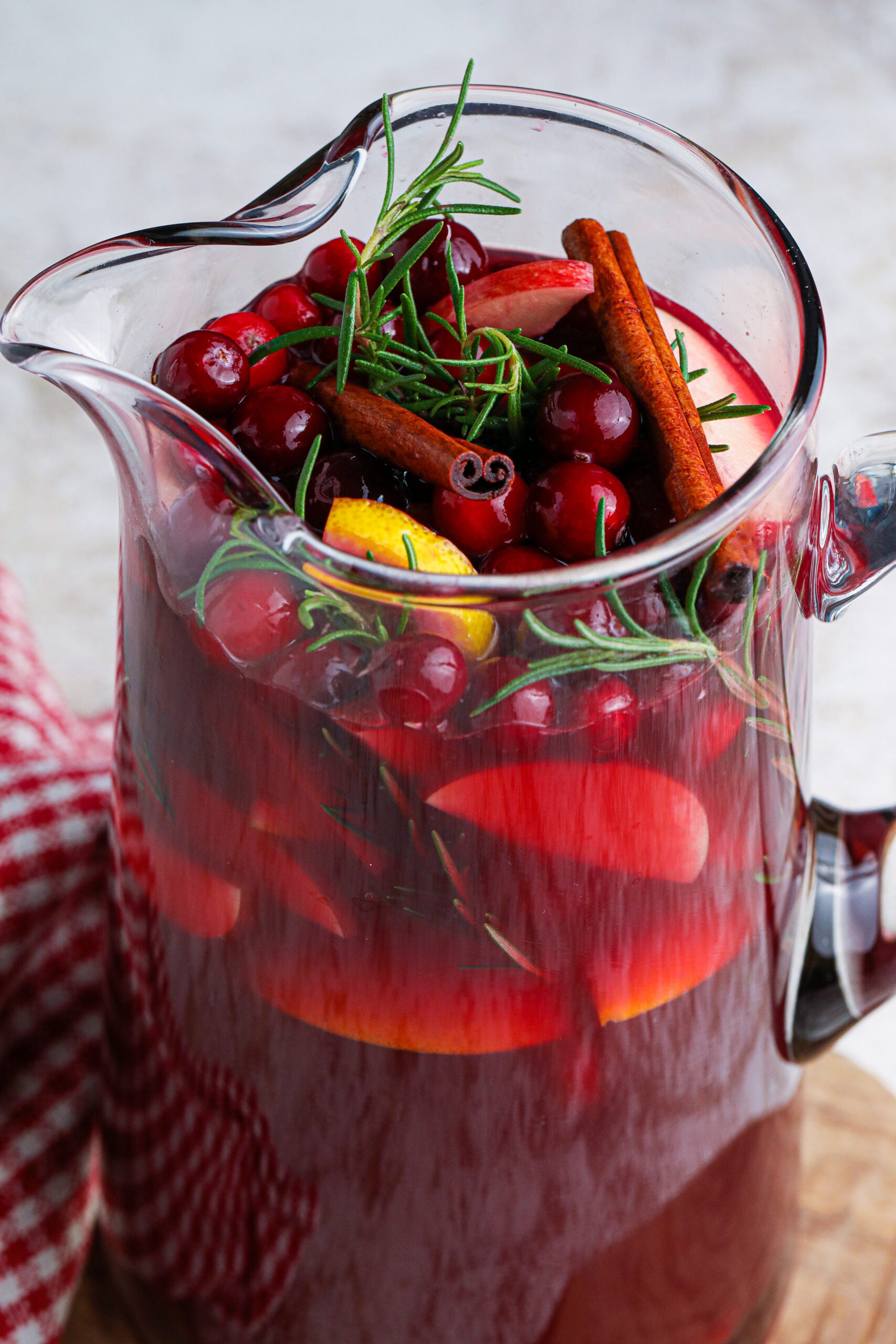 up close shot of red christmas sangria in a large glass clear pitcher filled with cranberries and cinnamon sticks