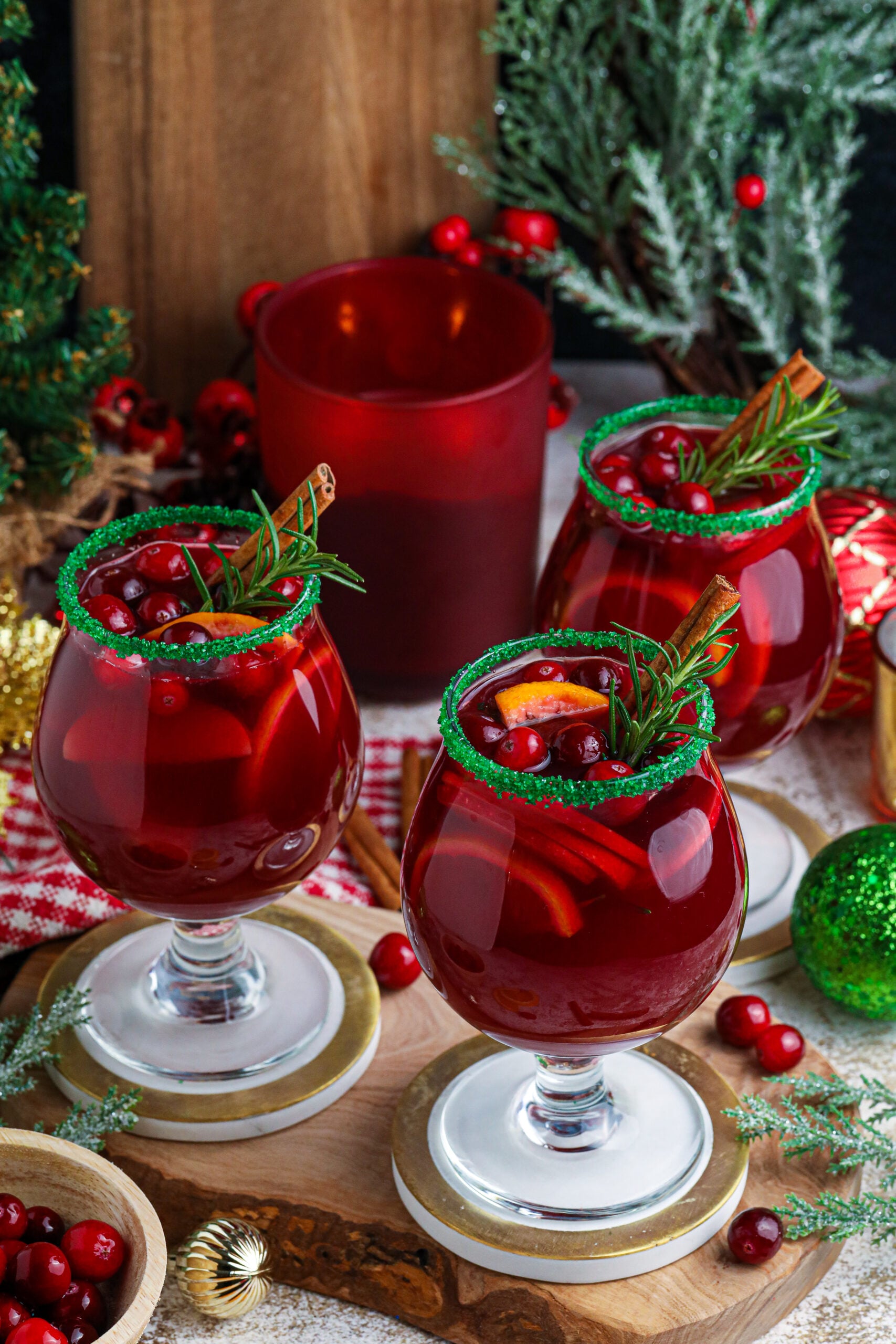 A photo of red christmas sangria in clear glasses with a green sugar rim on a wood table