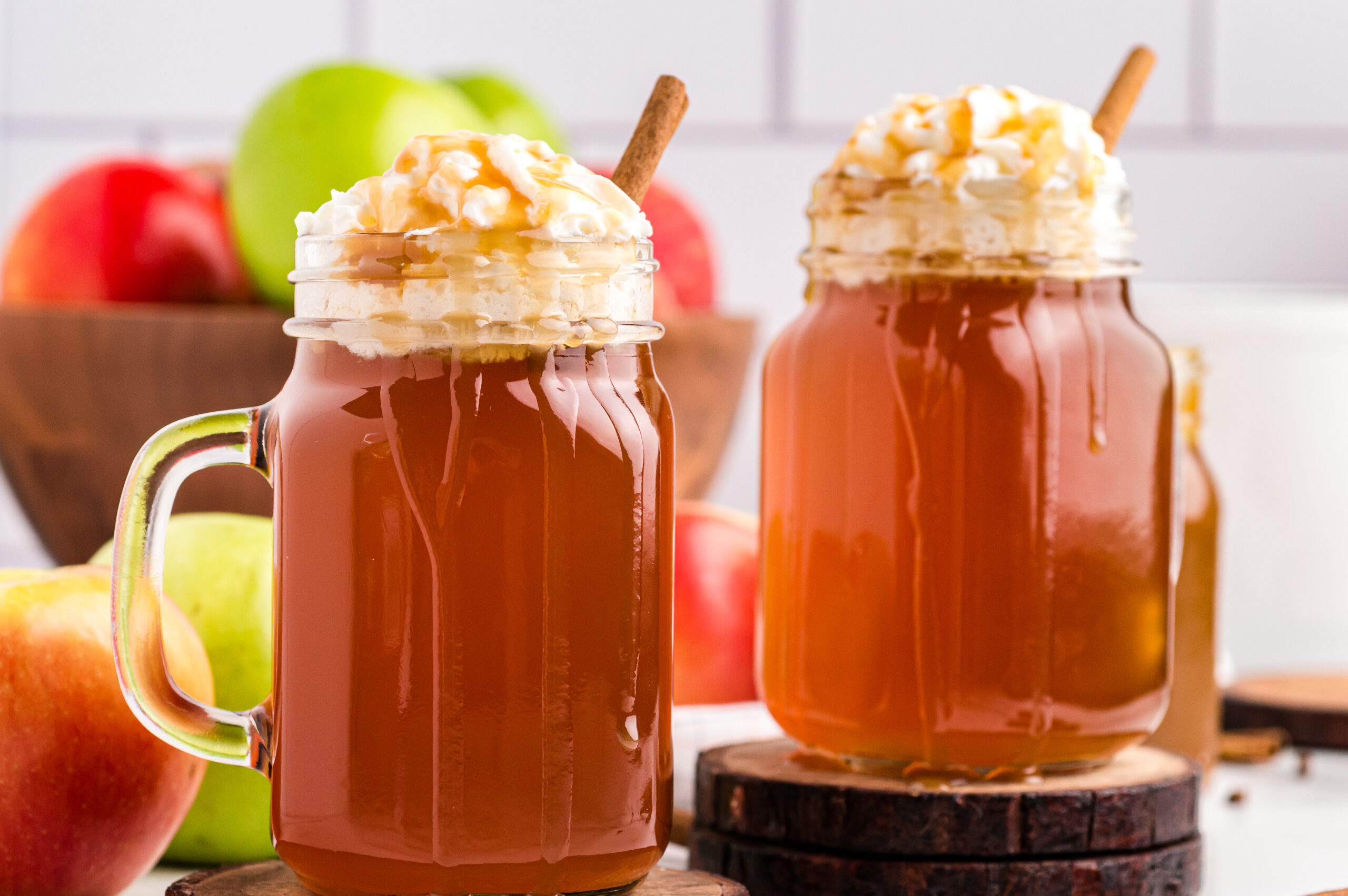 two Crock Pot Caramel Apple Ciders in a mason jars with whipped cream and syrup drizzled on top