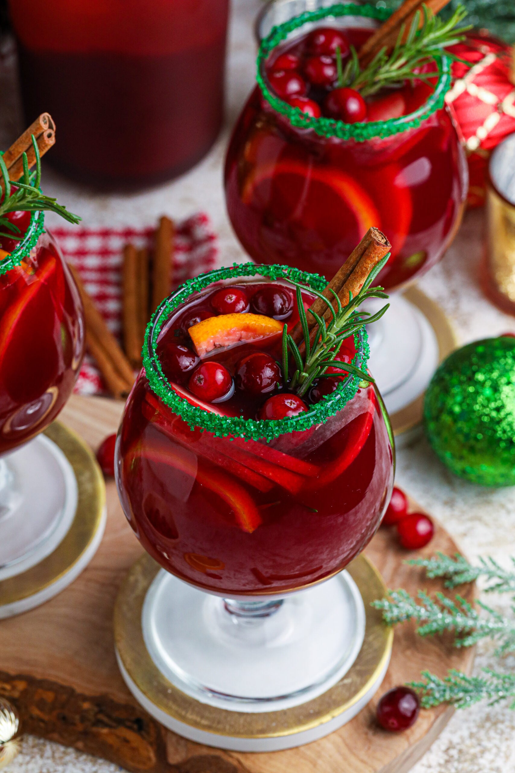 up close shot of red christmas sangria in clear glasses with a green sugar rim on a wood table