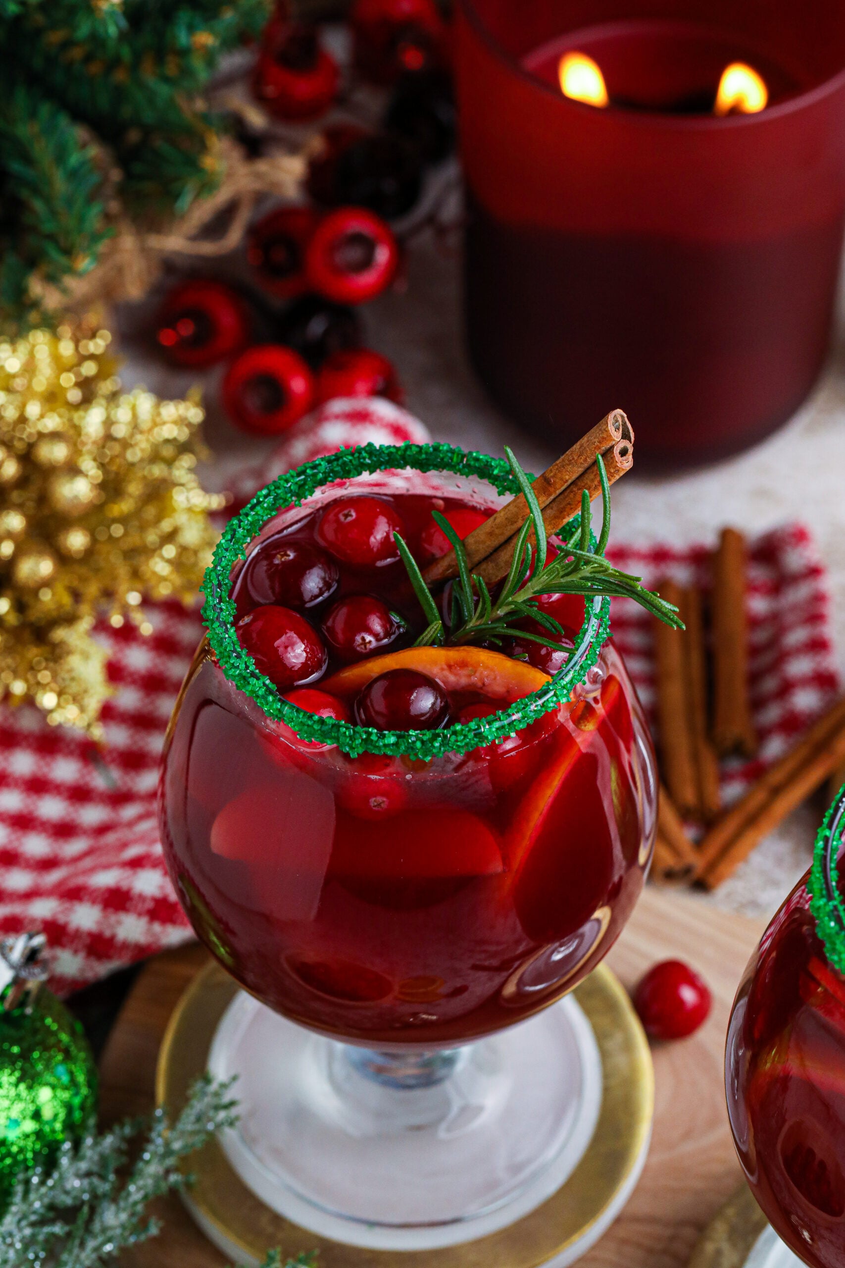 up close shot of red christmas sangria in a clear glass with a green sugar rim on a wood table with a candle lit in the background